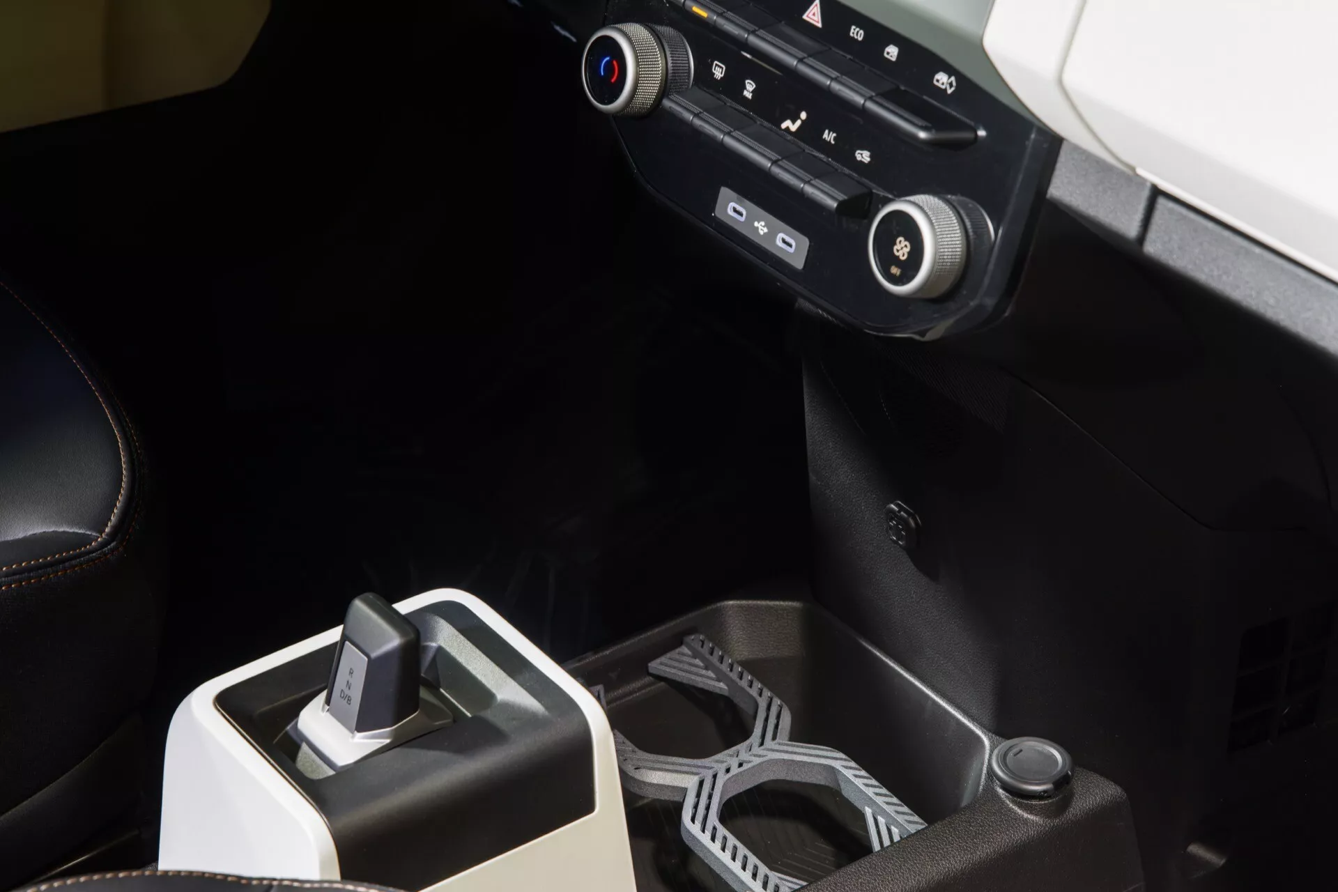Detail interiéru Dacia Spring 2024 po faceliftu s důrazem na centrální konzolu s elektronickým řazením, inovativními držáky nápojů a pokročilým systémem klimatizace, pohled z mírně zvýšeného úhlu zdůrazňující design a technologie