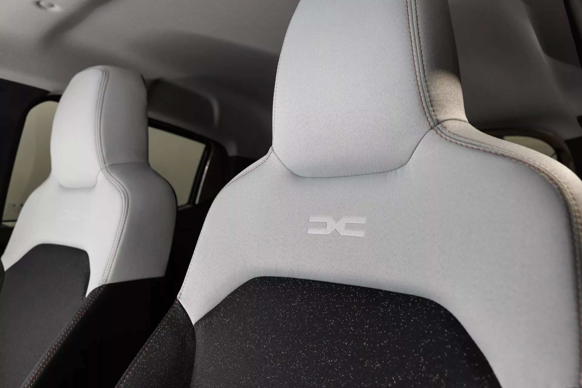 Interiér Dacie Spring 2024 s předními sedadly ve dvoutónovém designu a s vyraženým logem z pohledu ze zadního sedadla, zdůrazňující design a kvalitu látky