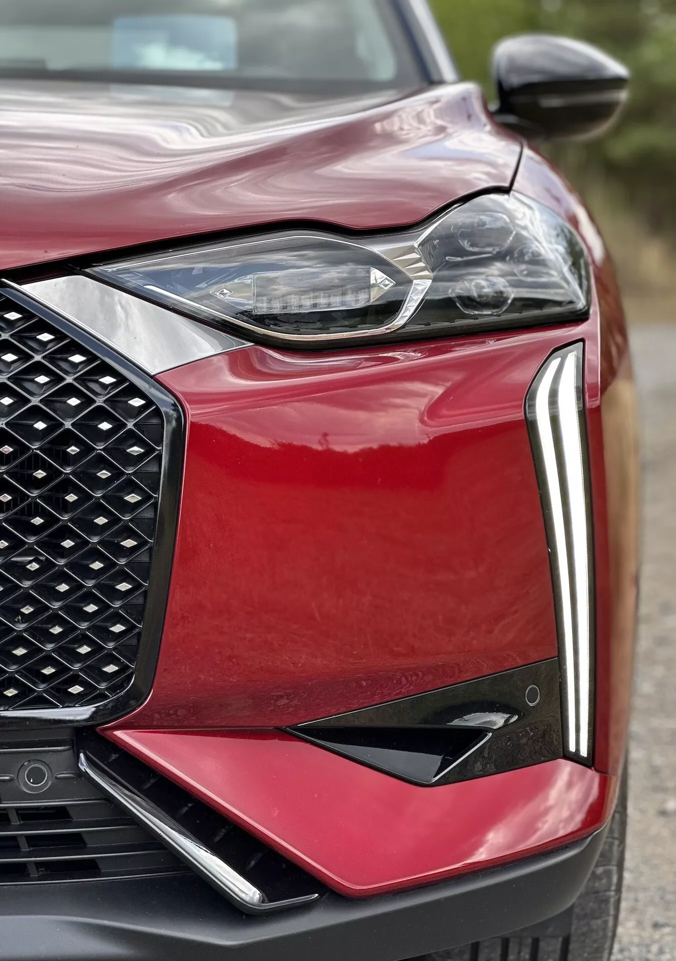 Detailní pohled na přední levou část DS Automobiles DS 3 E-TENSE 2023, zvýrazňující design LED světlometu, včelí plástev na mřížce chladiče, aerodynamickou kapotu a sportovní přední nárazník