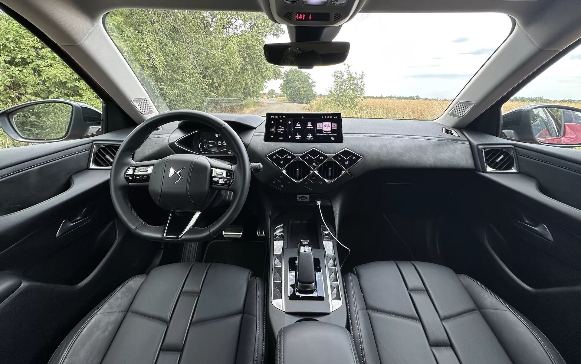 Interiérový pohled DS Automobiles DS-3 2023 ze zadního sedadla ukazující palubní desku, digitální přístrojový panel, multifunkční volant, dotykovou obrazovku infotainmentu, tlačítka klimatizace a luxusní kožená sedadla.