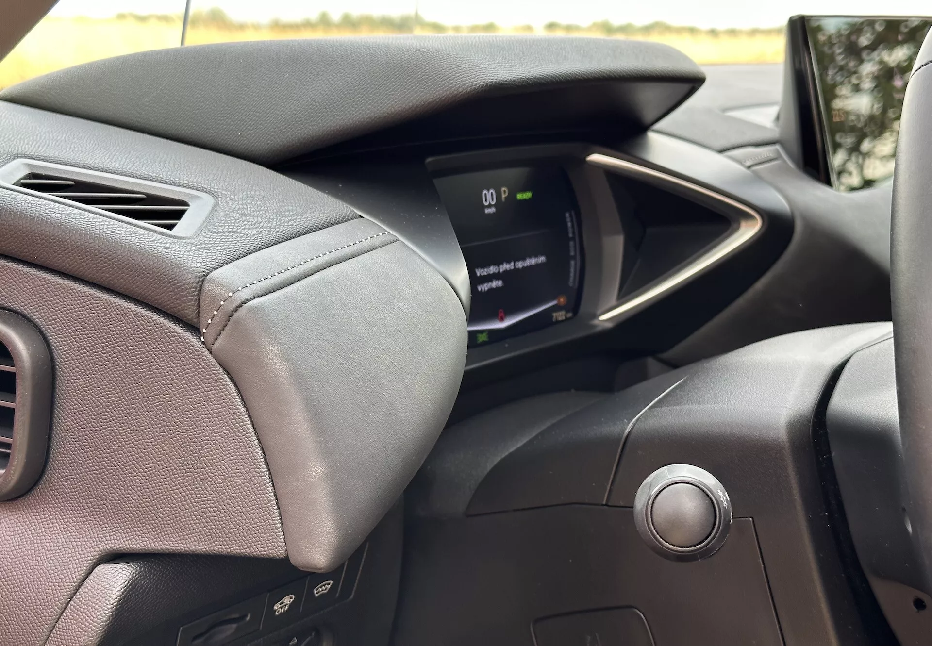 Interiérový pohled na DS Automobiles DS-3 E-TENSE 2023 zaměřený na palubní desku na straně řidiče, obsahující volant potažený koží se švy s ovládacími tlačítky, moderní digitální přístrojovou desku a systém startování tlačítkem, zdůrazňující pokročilou automobilovou technologii a ergonomii řízení.