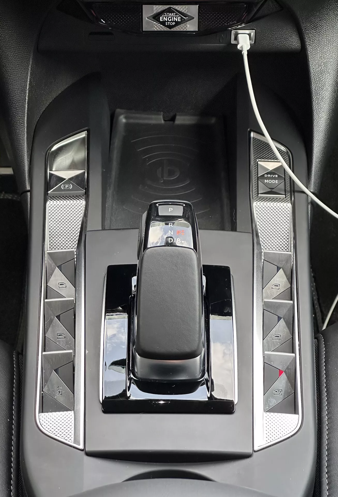 Detailní pohled na středovou konzoli DS 3 E-TENSE 2023 zobrazující elegantní automatickou řadicí páku se chromovým lemem, lesklé černé povrchy a tlačítka pro pokročilé funkce řízení