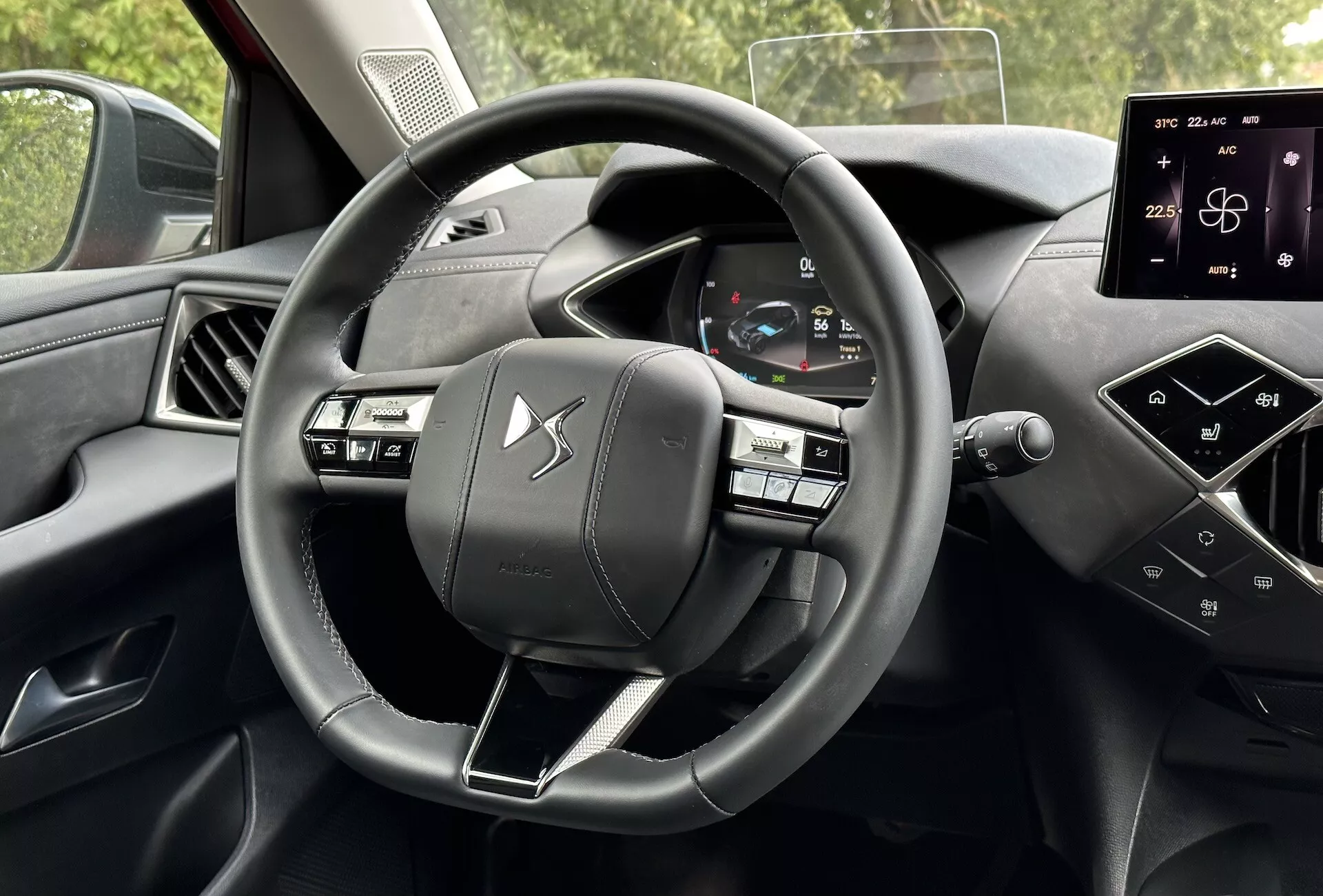 Interiér vozidla DS Automobiles DS-3 2023 (DS-3 E-TENSE) z pohledu řidiče s trojramenným volantem s multifunkčními tlačítky, digitálním přístrojovým panelem zobrazujícím rychlost vozidla a diagnostiku a interaktivním dotykovým displejem na středové konzoli pro navigaci a nastavení vozidla, který předvádí moderní automobilovou technologii a prvky prémiového designu.