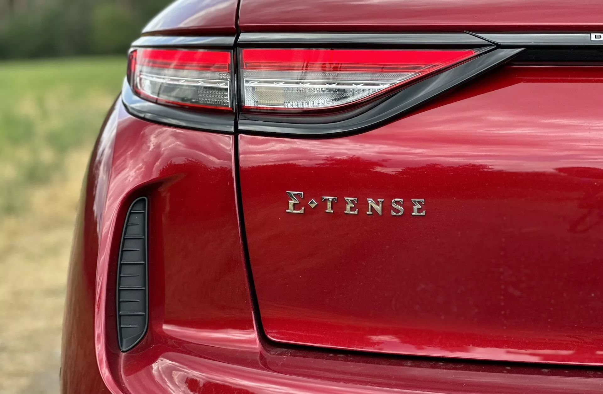 Detailní pohled na zadní levou stranu DS Automobiles DS-3 E-TENSE 2023 s LED zadním světlem, označením E-TENSE, lesklým červeným lakem, prvkem vzduchového sání a detailním zpracováním v přírodním venkovním prostředí