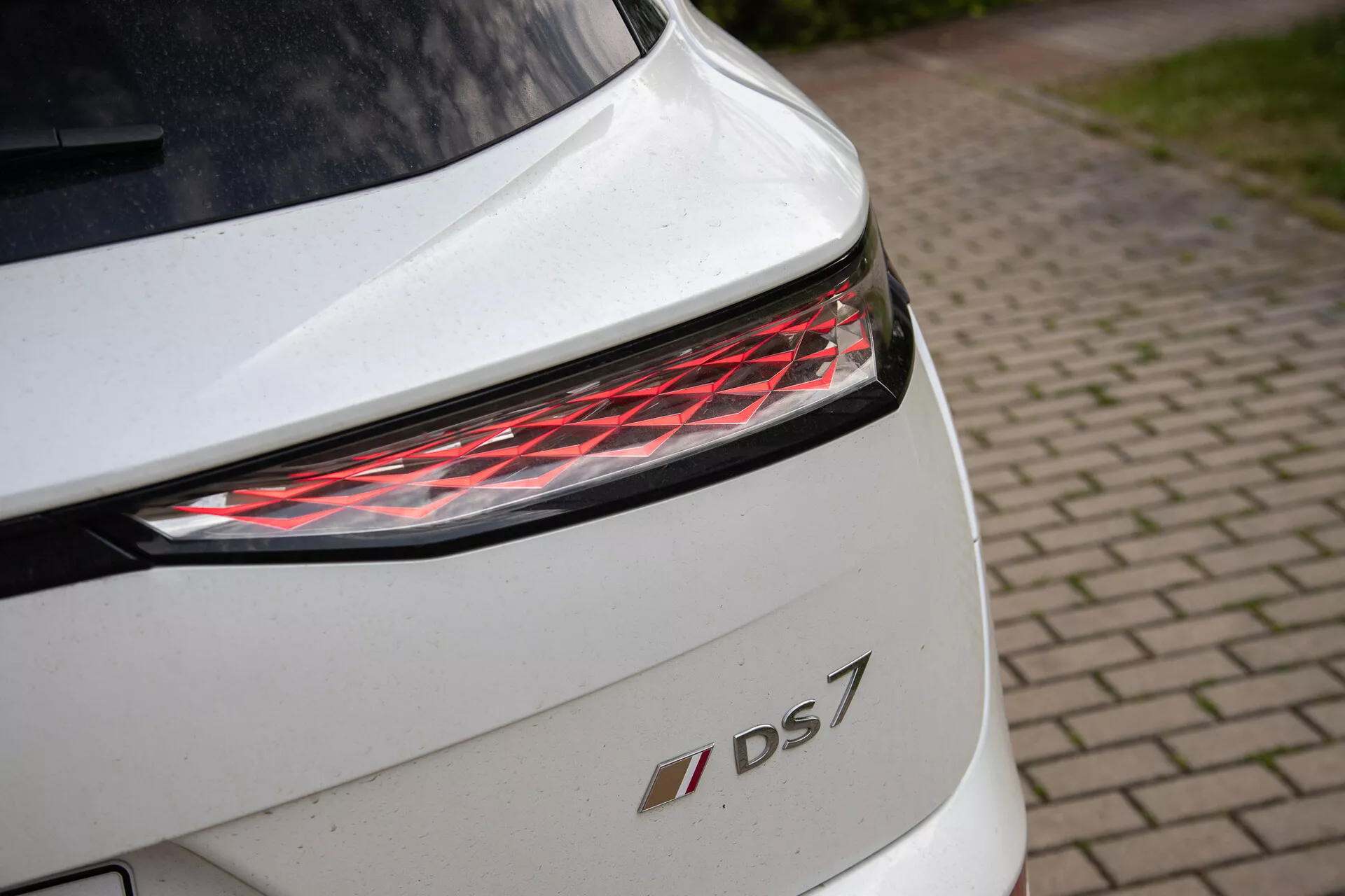 Detailní záběr zadní části bílého DS 7 s moderním LED zadním světlem a emblémem modelu, zdůrazňující designové prvky a prémiové provedení
