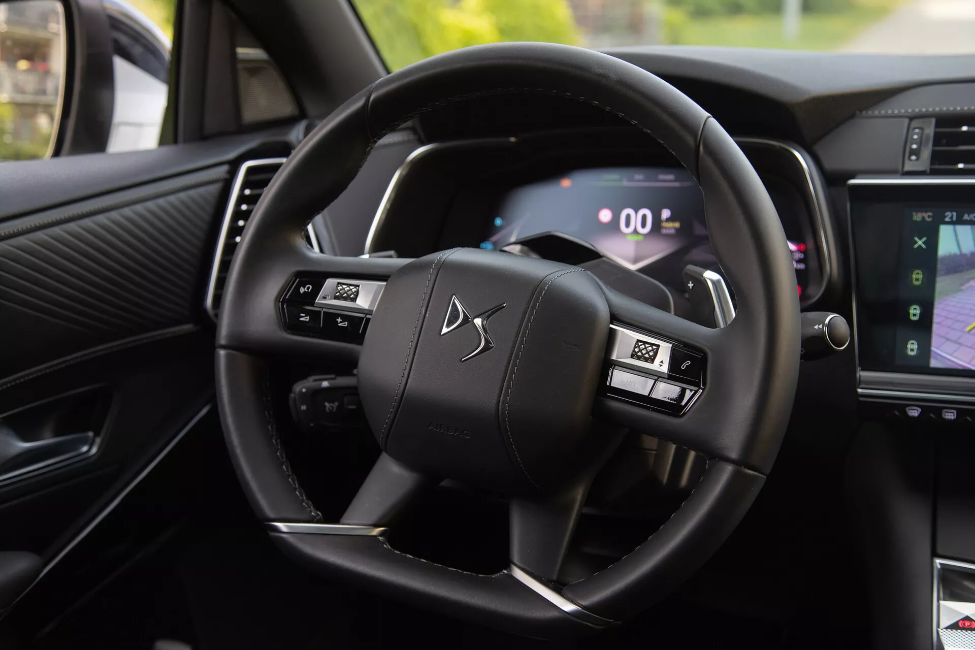 Interiérový pohled na DS Automobiles DS-7 2022 zobrazující volant s multifunkčními tlačítky a digitální přístrojovou desku, včetně páček řazení za volantem a části systému infotainment zobrazující navigaci
