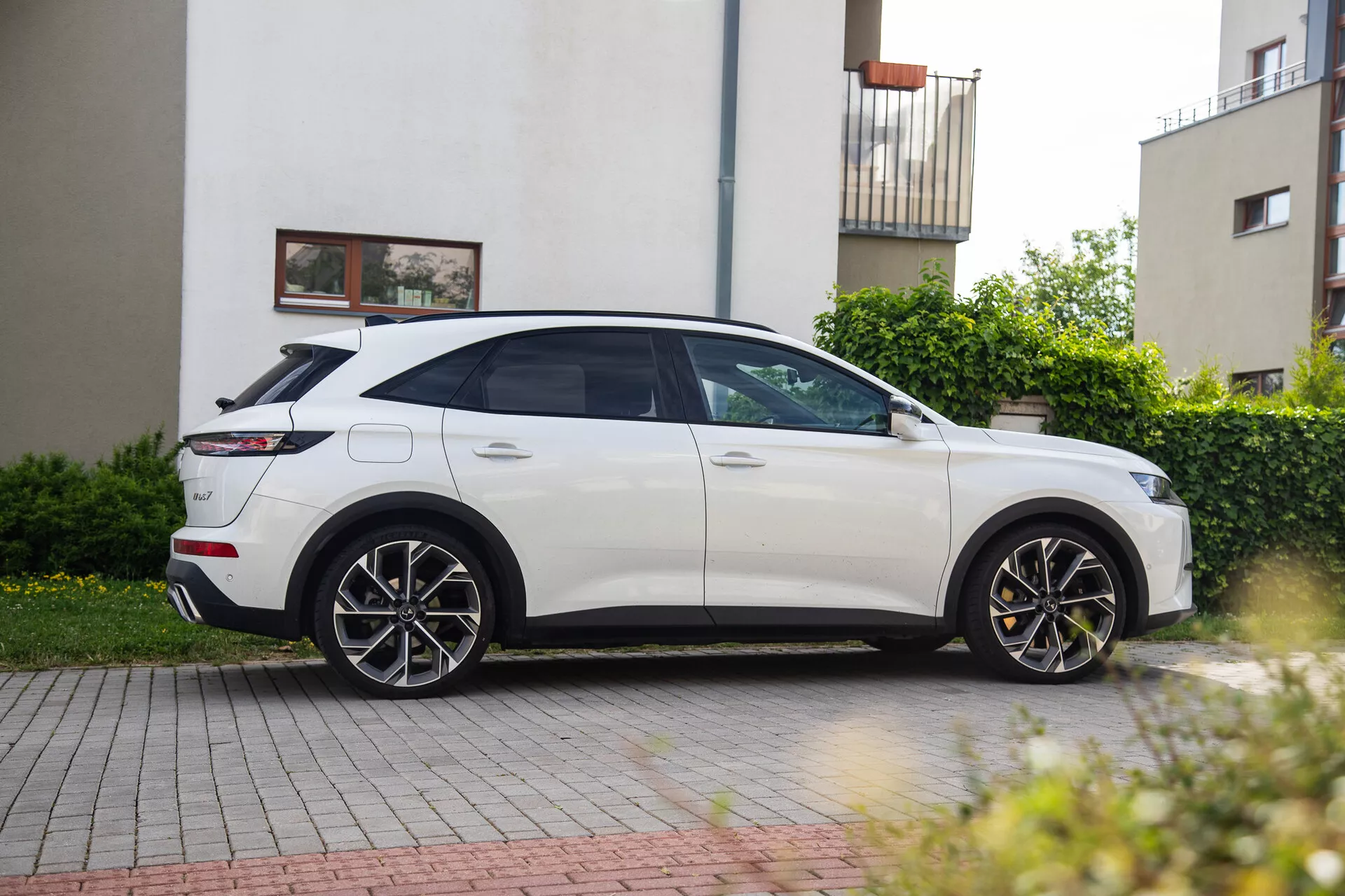 Bílý SUV DS Automobiles DS-7 rok 2022 profilový pohled ze strany zaparkovaný na příjezdové cestě v rezidenční oblasti ukazující elegantní design, aerodynamické linie, velká slitinová kola, LED světlomety, boční zrcátka a panoramatické střešní okno
