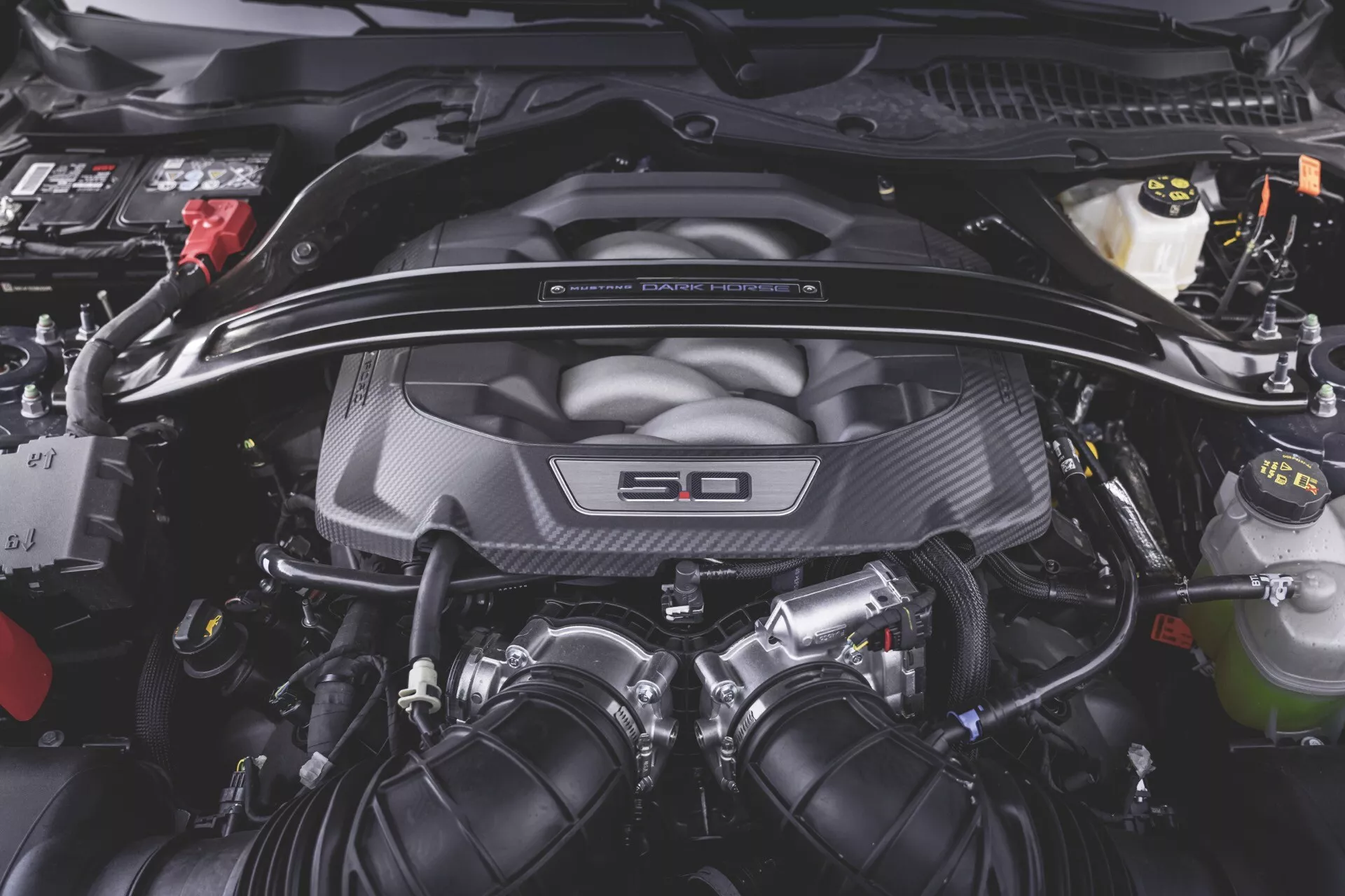 Detailní pohled na motorový prostor Ford Mustang 2. generace 2024 s 5,0litrovým motorem V8, krytem motoru z uhlíkových vláken, zásobníky kapalin a elektrickým vedením