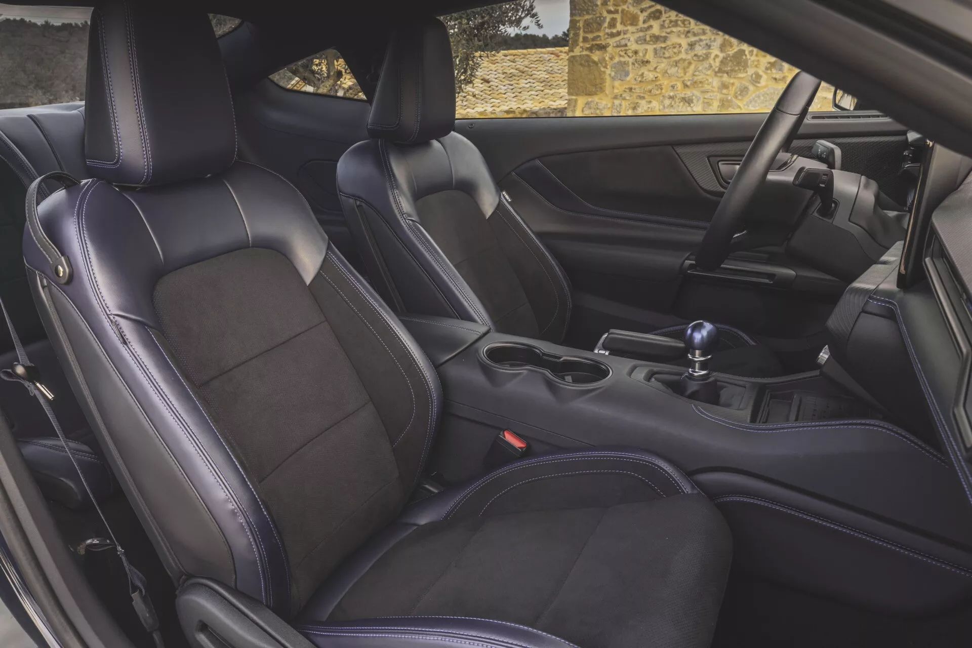 Detailní pohled na interiér Ford Mustang 2024 se zaměřením na sportovní sedadla z prémiové kůže, ruční řadicí páku a středovou konzolu z perspektivy dveří řidiče