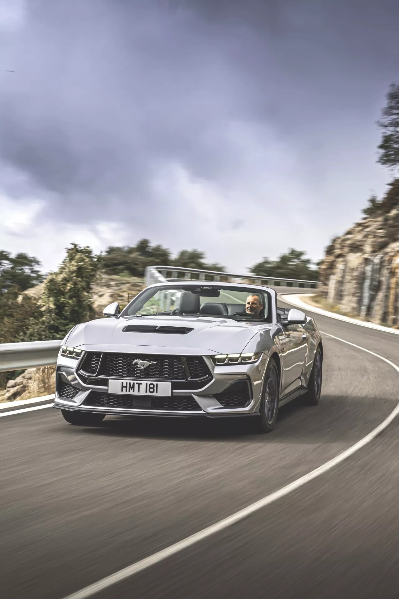 Ford Mustang 2024 2. generace kabriolet v dynamické jízdě na klikaté silnici s LED světlomety, charakteristickou maskou, sklopenou střechou s viditelným interiérem a řidičem, navrženo pro výkon a luxus