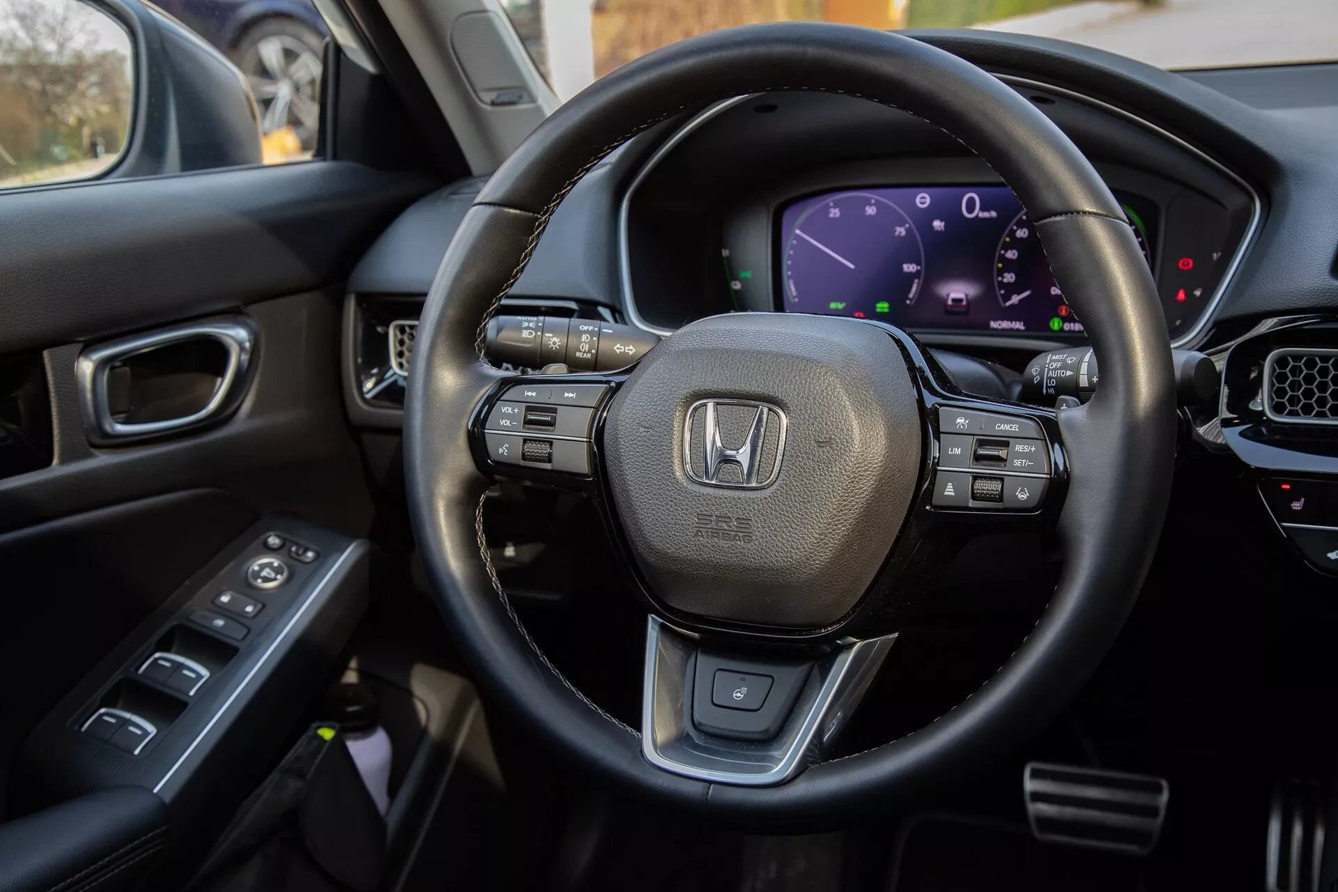 Vnitřní pohled Honda Civic 2022 z místa řidiče, zdůrazňuje volant obšitý kůží s multifunkčními ovladači, digitální přístrojovou desku, část středové konzoly s dotykovým displejem a ovládání na dveřích řidiče pro komplexní zobrazení moderních technologických funkcí a luxusního designu vozidla.