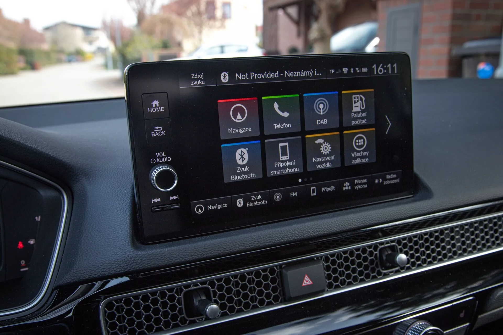 Interiér Honda Civic 2022 ukazuje moderní dotykový informační systém s navigací, ikonami pro přehrávání audia a médií, připojením telefonu, DAB, informacemi o stavu vozidla, Bluetooth a možnostmi nastavení vozidla, proti texturované palubní desce s včelí pláství.