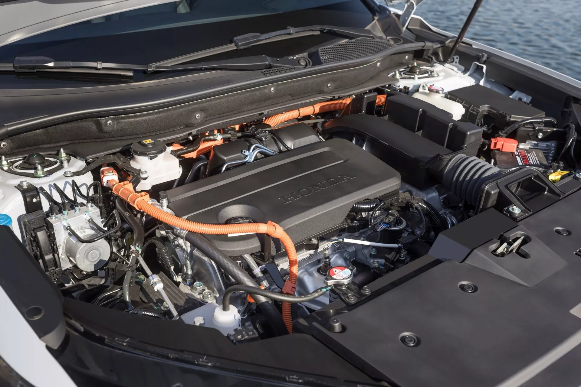Detailní pohled na hybridní motor a komponenty Honda CR-V 6. generace z roku 2023, s vysokonapěťovými kabely a krytem motoru označeným Toyota, ukazující kombinaci spalovacího a elektrického vozidlového technologie