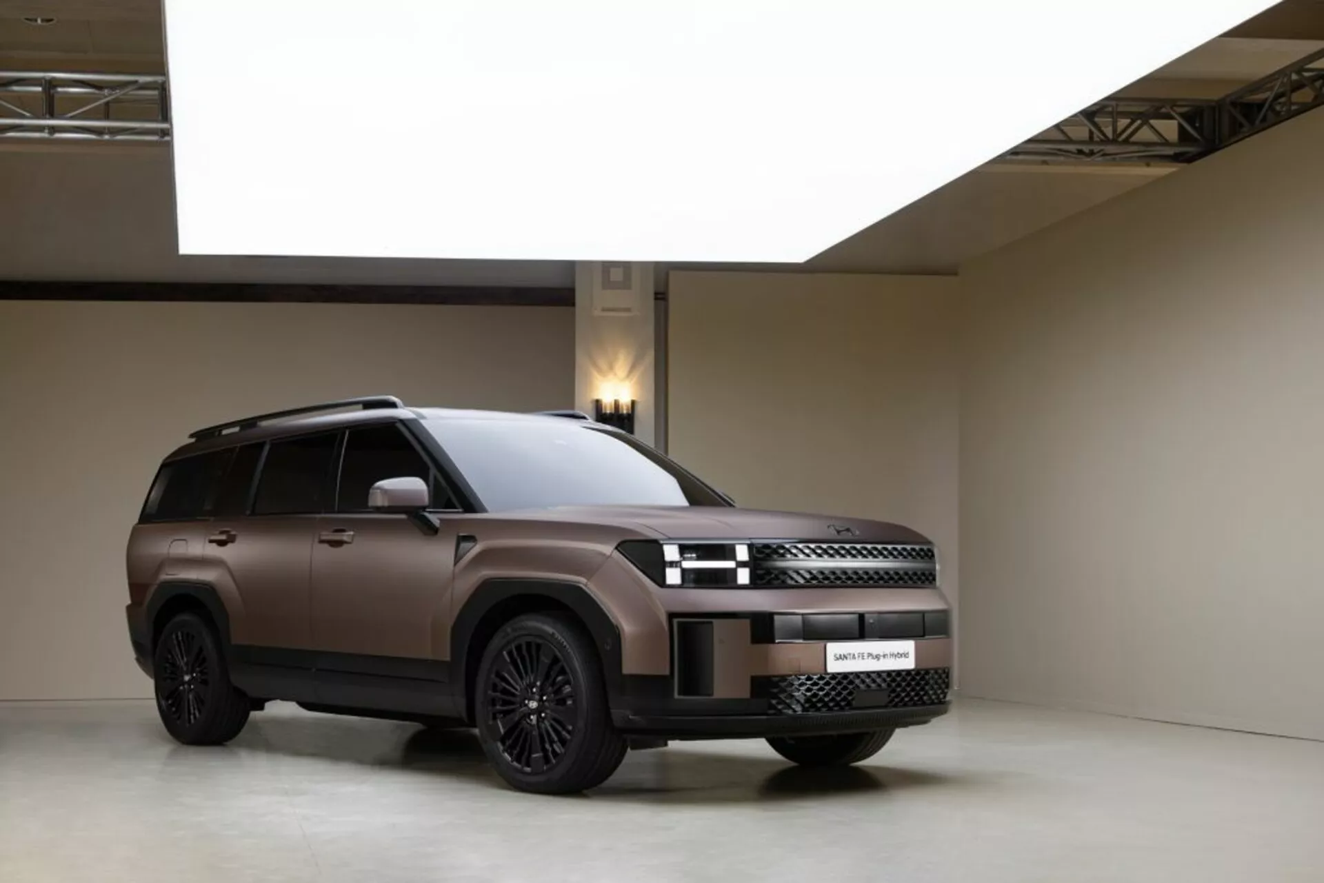 Studiová fotografie vozu Hyundai Santa-Fe 2024 (5. generace) z třechčtvrtinového předního pohledu ukazujícího jeho moderní design. Vůz obsahuje propracovanou přední masku s elegantními LED světly a přední nárazník s integrovanými senzory. Boční pohled zvýrazňuje velká litá kola, střešní nosiče, tónovaná okna a boční schůdek. Matný lak je zvýrazněn kontrolovaným studiovým osvětlením, které podtrhuje luxusní a robustní vzhled SUV na minimalistickém pozadí.