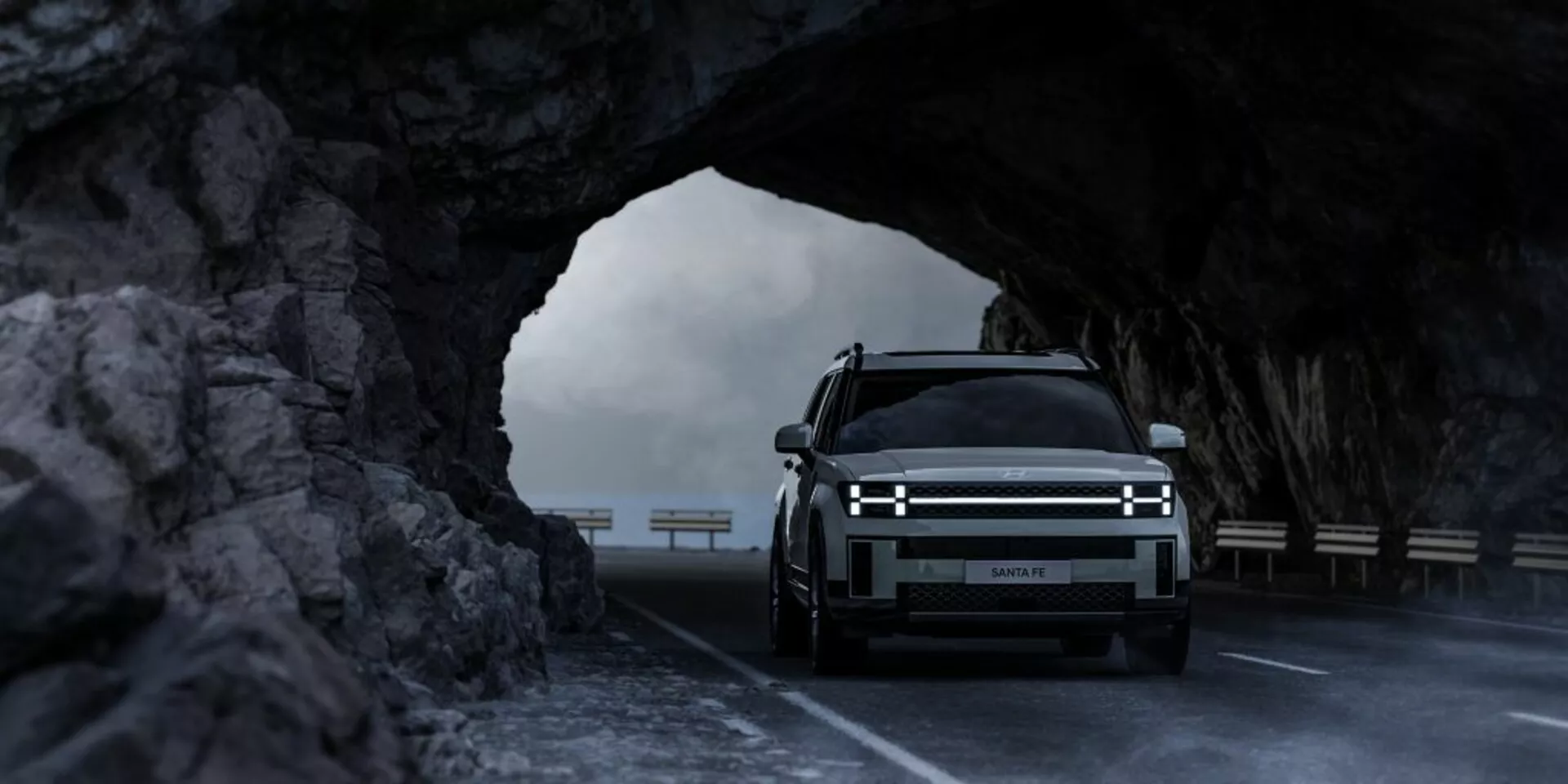 Přední pohled na Hyundai Santa Fe 2024 (5. generace) v tunelu vyřezaném do skály, zvýrazňující horizontální LED světlomety, velkou přední mřížku značíci případný elektrický model a luxusní design s osvětleným logem, zachycený v jemném světle, zdůrazňující jeho robustní, off-road potenciál.