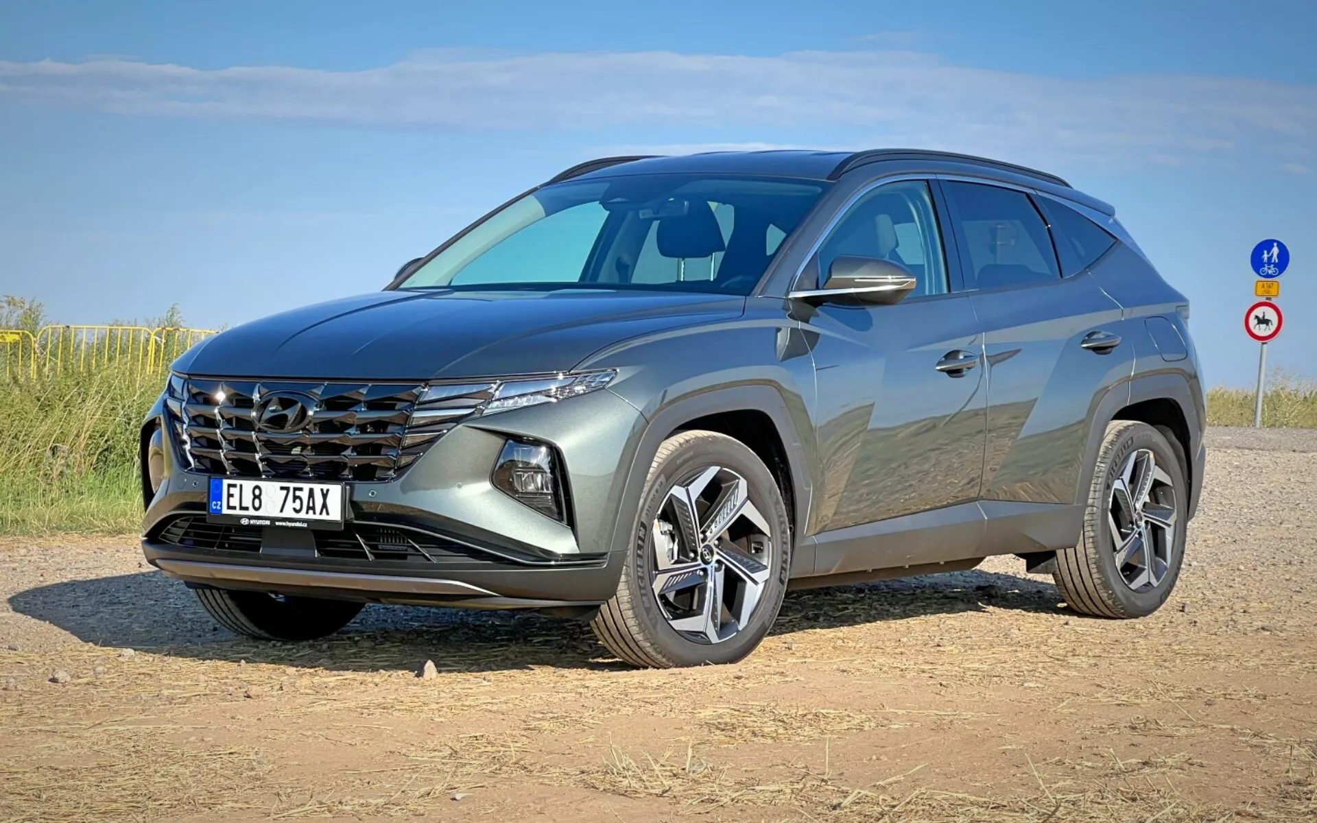 Moderní SUV Hyundai Tucson 2020 zobrazené ze tříčtvrtečního předního úhlu, předvádějící jeho výraznou mřížku chladiče, elegantní světlomety, přední část, sochařsky vytvarovanou kapotu a slitinová kola na nezpevněné odstavné ploše pod jasnou oblohou