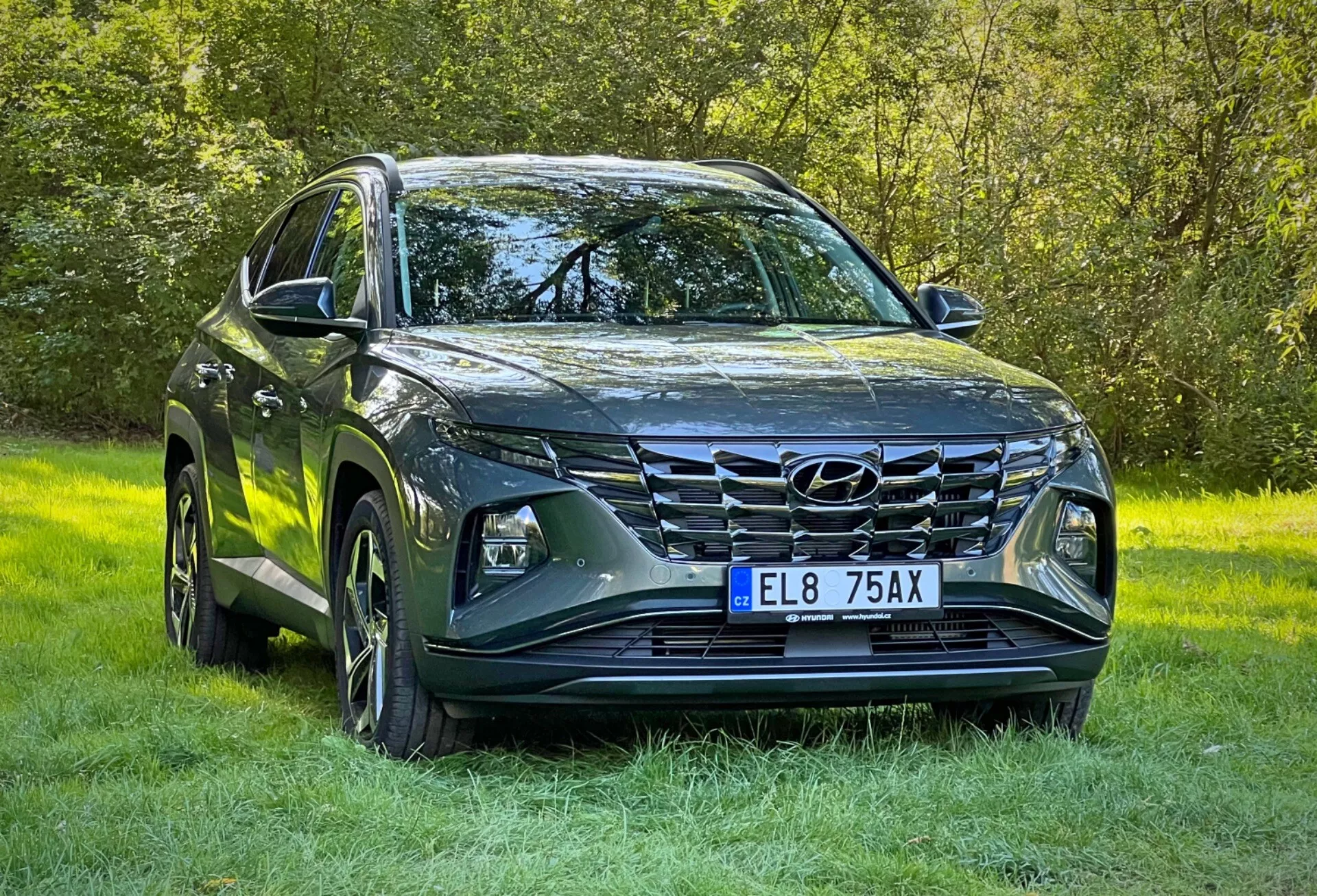 SUV Hyundai Tucson 2020 v metalickém provedení, předvádějící LED světlomety, výraznou přední mřížku, sochařsky zpracovanou kapotu, slitinová kola a boční zrcátka s integrovanými směrovými signály, zaparkované na trávě zdůrazňující jeho schopnost jízdy v terénu