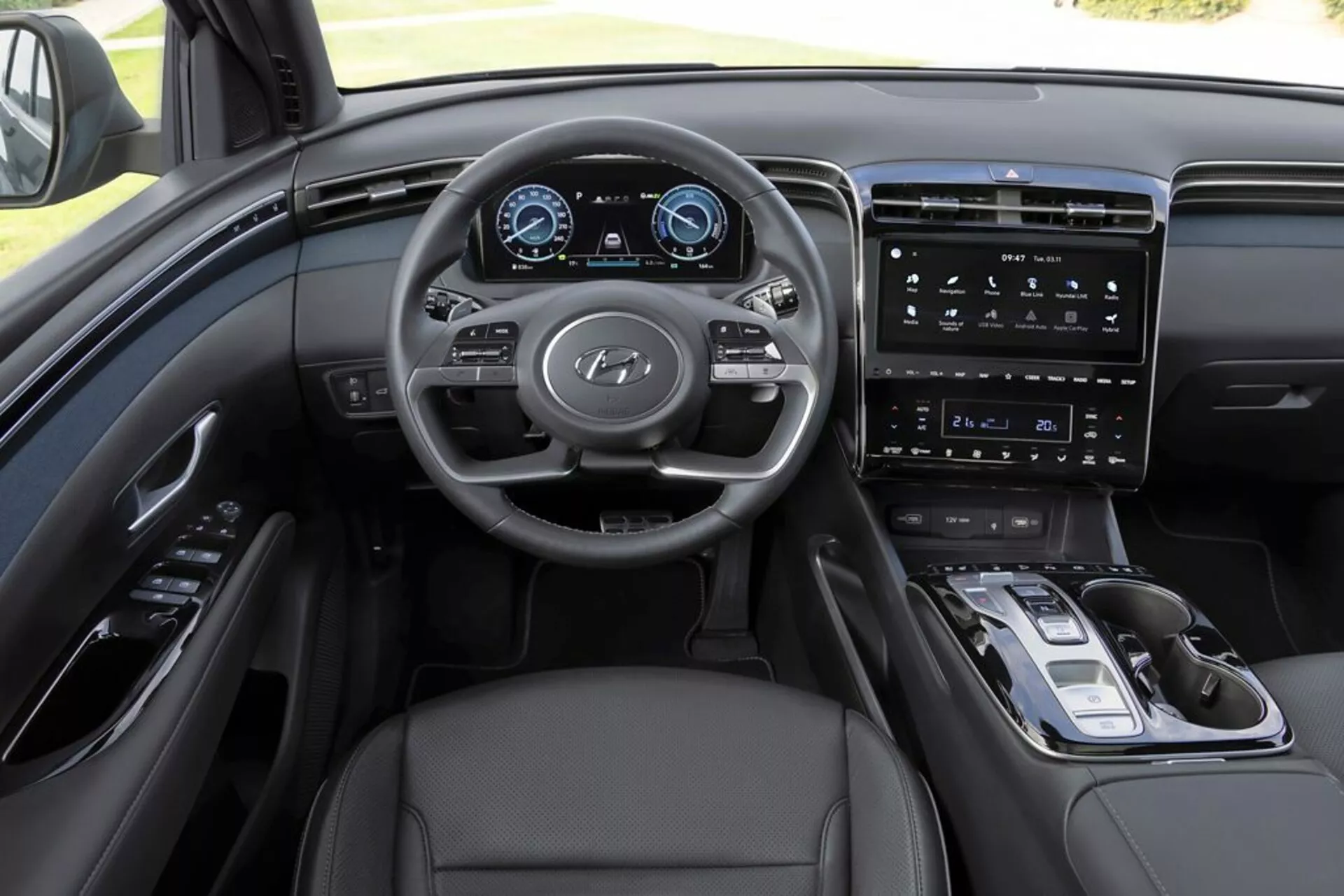 Interiér Hyundai Tucson 2020 z pohledu řidiče, zdůraznění palubní desky, multifunkčního volantu s logem Hyundai, plně digitálního přístrojového panelu, vertikálního dotykového informačního systému, minimalistických ovládacích prvků na středové konzole, elektronického voliče převodovky, čalounění z kůže a sofistikovaného monochromatického barevného schématu