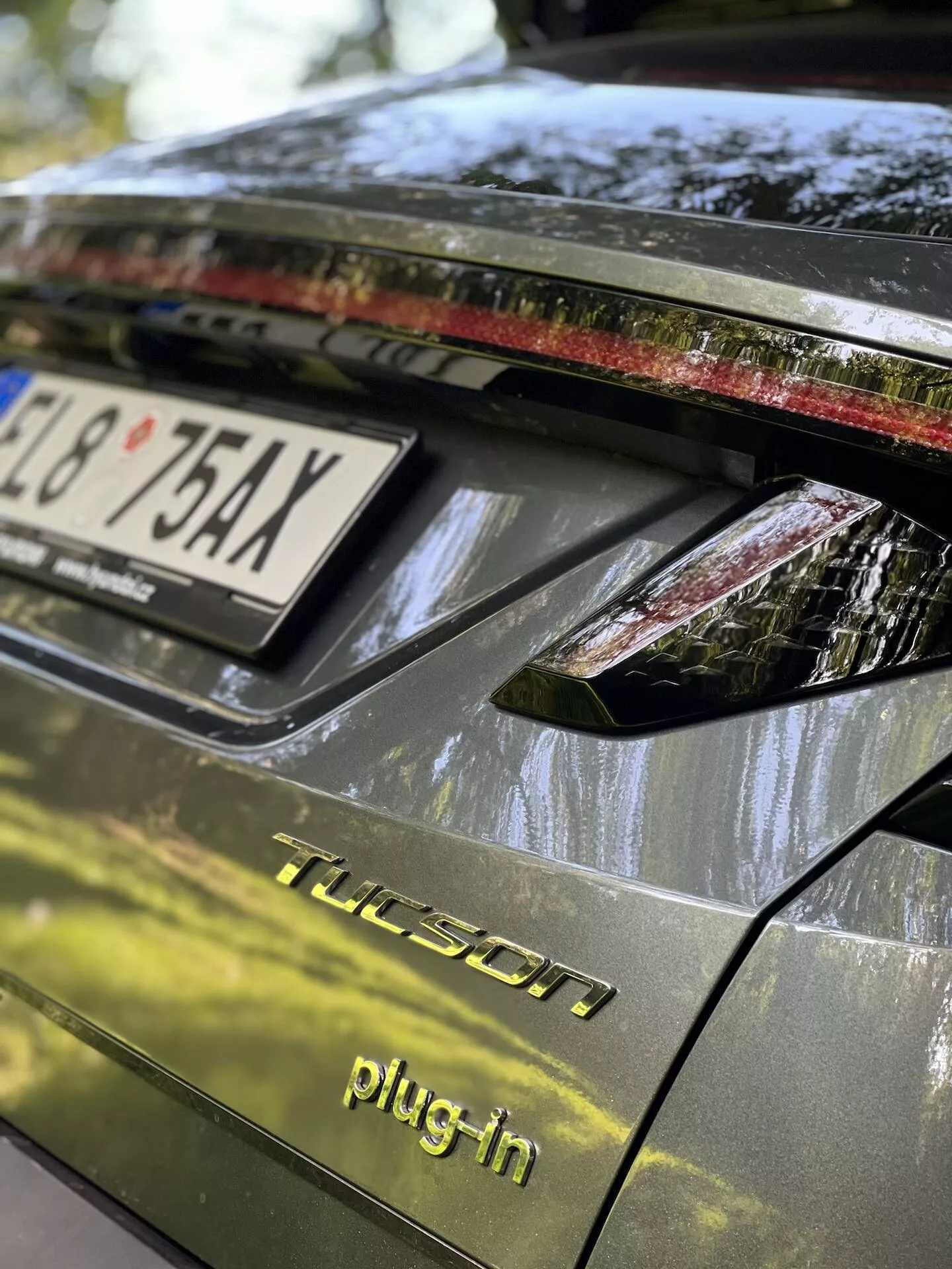 Detailní pohled na zadní část vozu Hyundai Tucson 2020 ve verzi plug-in hybrid, zahrnující víko kufru, zadní světelnou soupravu s LED světly, tmavý lesklý povrch a detaily naznačující parkování v exteriéru