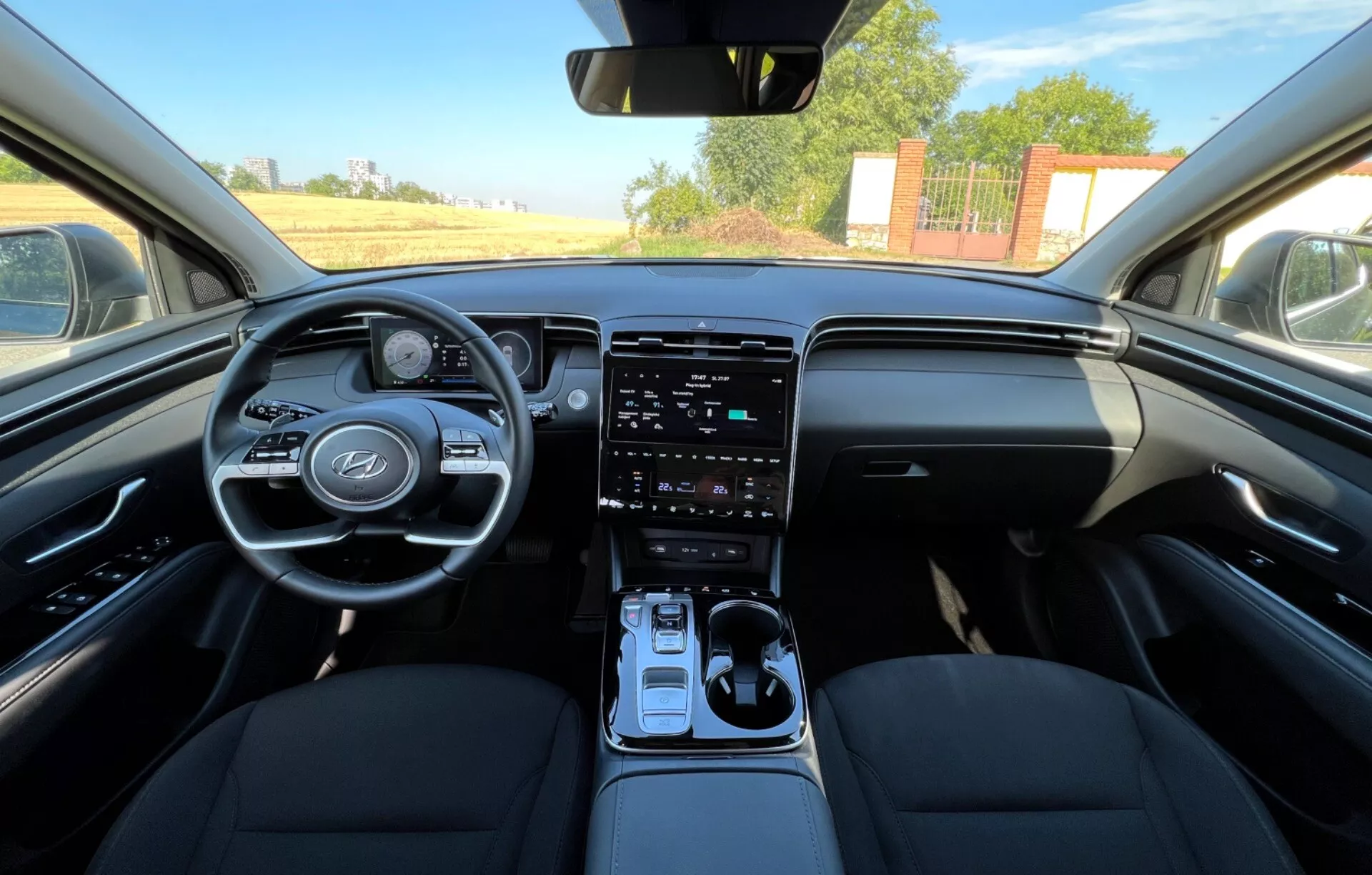 Interiér Hyundai Tucson 2020 ukazující přední sedadla, volant s logem výrobce a ovládacími tlačítky, digitální přístrojový panel, vertikální dotykový infotainment systém na středové konzole, automatickou řadicí páku a design palubní desky ve dvoutónovém provedení z pohledu řidiče