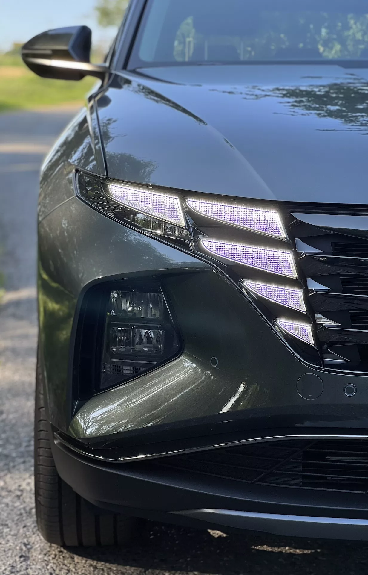 Detailní úhlový pohled na Hyundai Tucson 2020 ukazující složitý design LED světlometů a část přední mřížky s lesklým povrchem za slabého osvětlení, ilustrující funkce luxusních vozů a moderní technologii automobilového osvětlení.