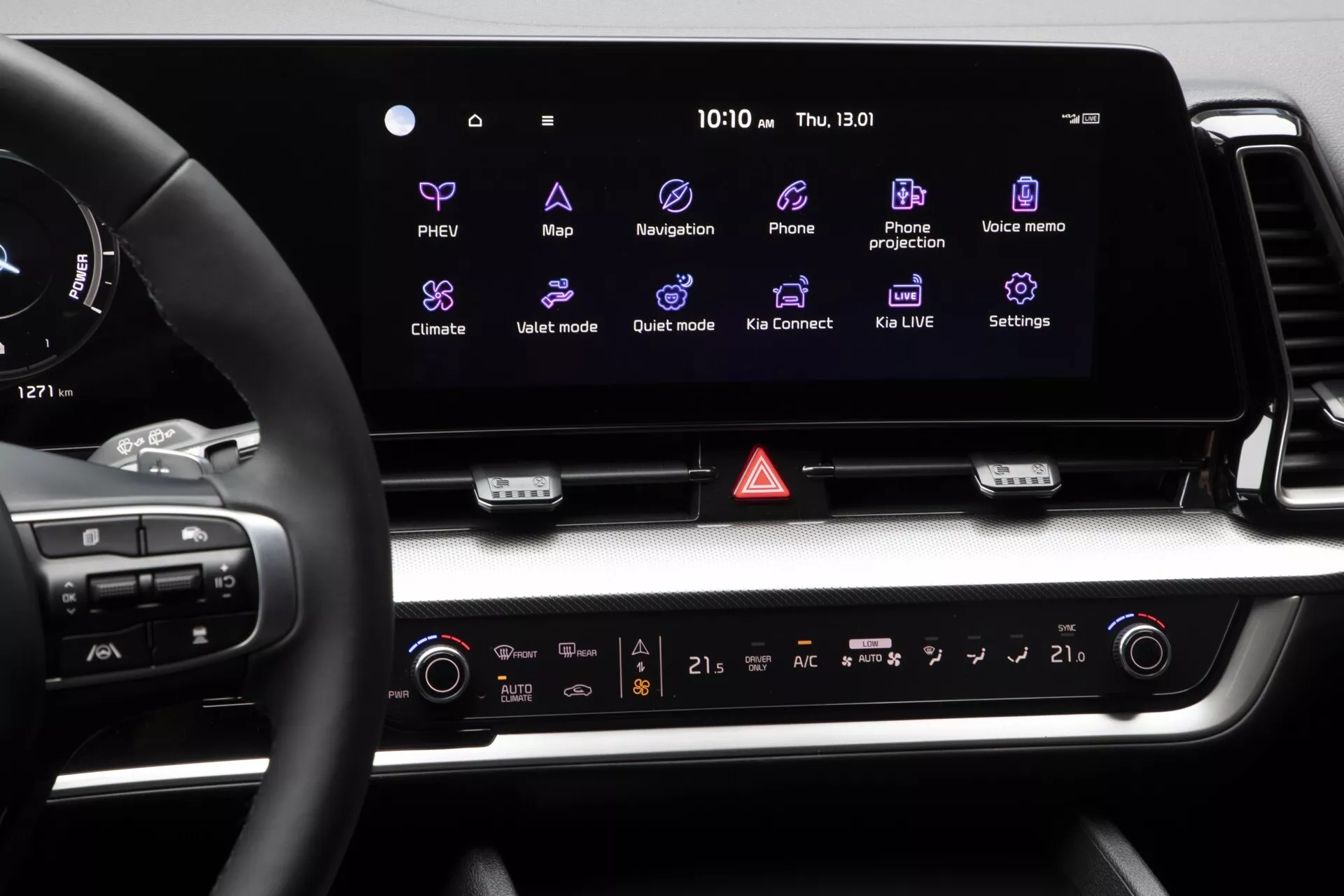 Interiér Kia Sportage NQ5 2022 s pohledem na palubní desku, zaměřený na displej informačně-zábavního systému a ovládací systém včetně stavu PHEV, klimatizace pro dva pásma, tlačítka výstražných světel a části volantu, zdůrazňující digitální a fyzické body interakce pro pohodlí řidiče.