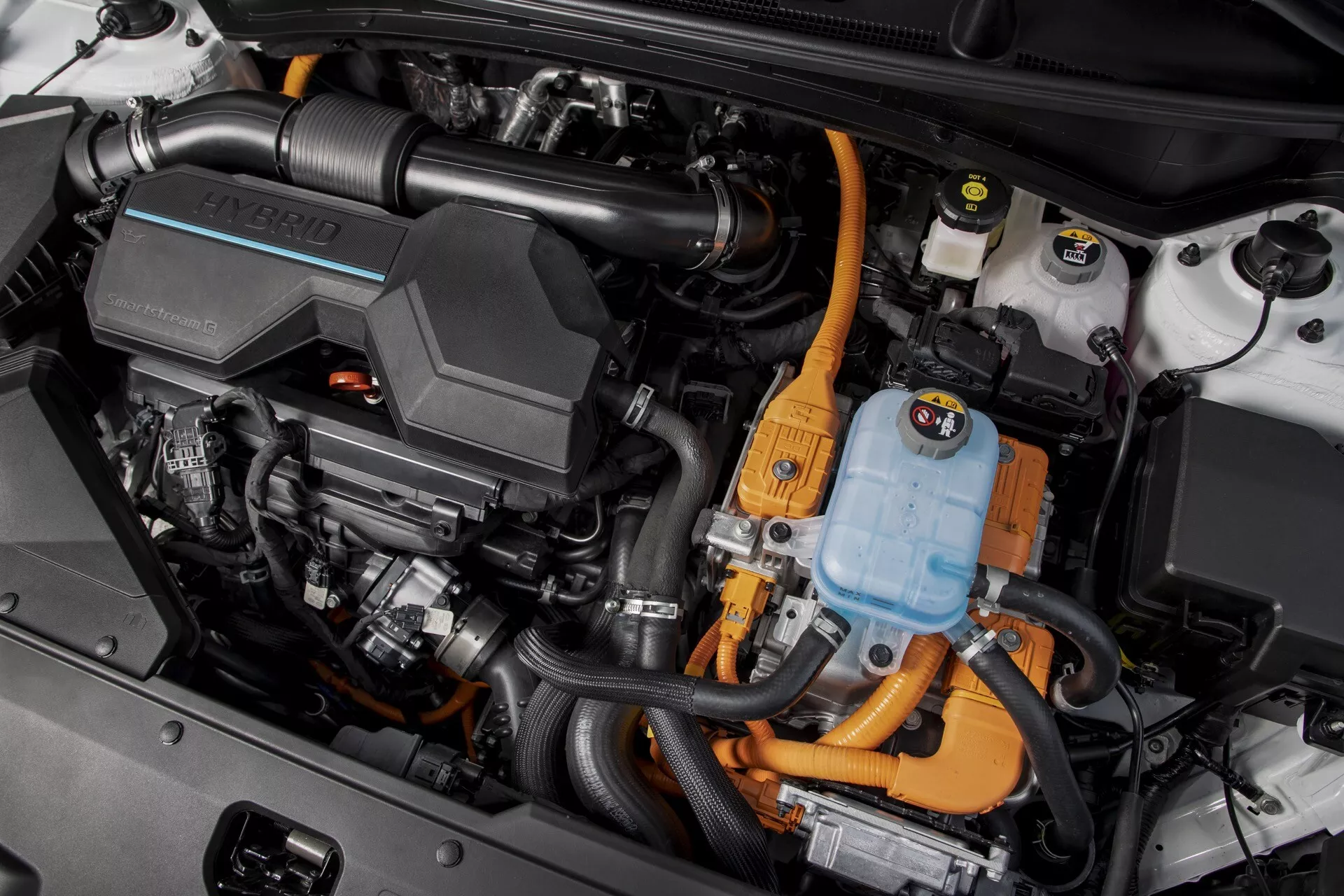 Detailní pohled na hybridní motorový prostor Kia Sportage 2022 NQ5, s vysokonapěťovým napájecím kabelem, střídačem, blokem motoru a různými součástmi hybridního pohonu