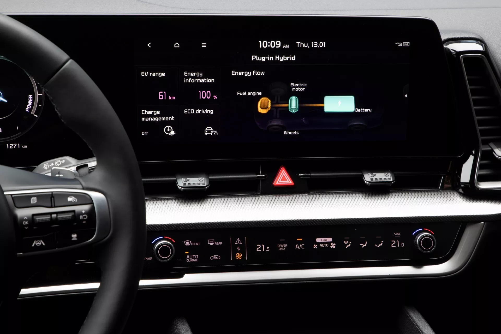Interiér palubní desky Kia Sportage NQ5 2022 s pokročilým displejem informačního systému s indikátory technologie plugin hybrid, dotykově citlivými ovladači klimatizace a ovládacími prvky na volantu pro pohodlí a bezpečnost řidiče, obklopenými materiály vysoké kvality s luxusními designovými akcenty