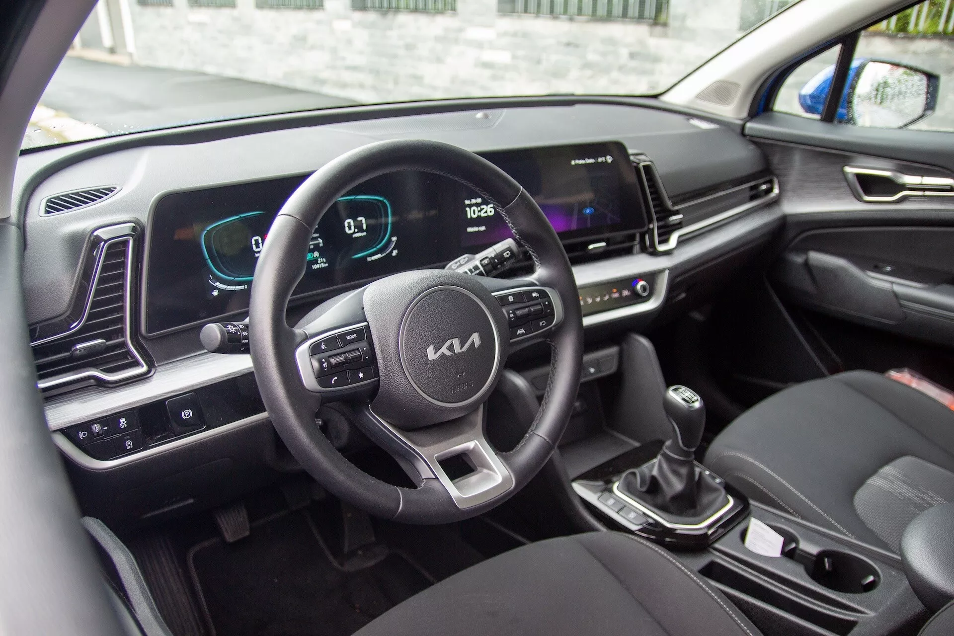 Interiér Kia Sportage 2022 s volantem s ovládacími tlačítky, digitálním přístrojovým panelem a obrazovkou infotainmentu