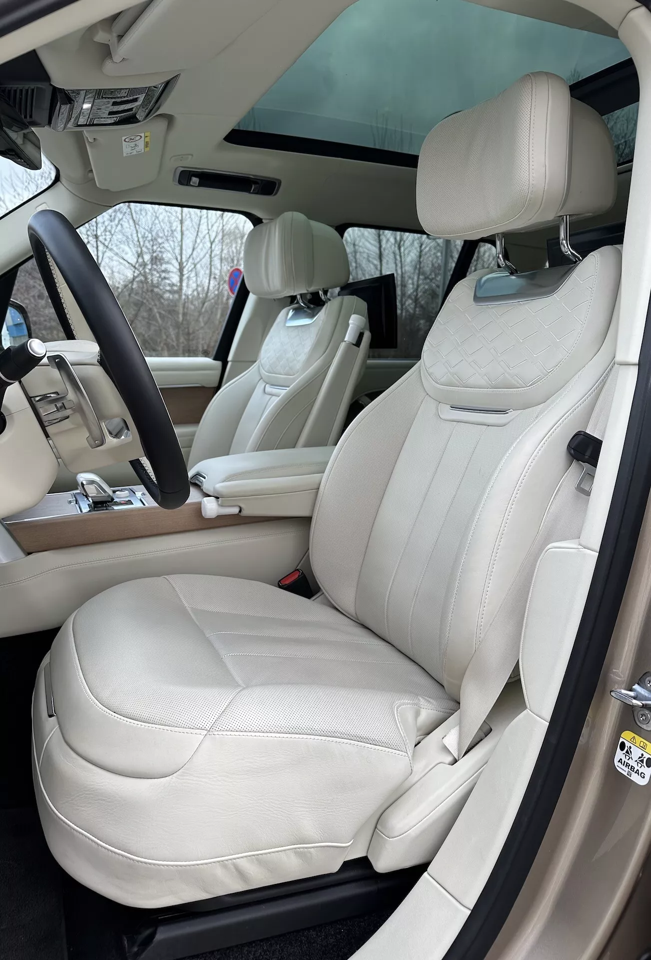 Interiér Land Rover Range Rover 2021 s výhledem na stranu řidiče, luxusní sedadla z krémové kůže, multifunkční volant a pokročilé ovládací prvky na středové konzoli