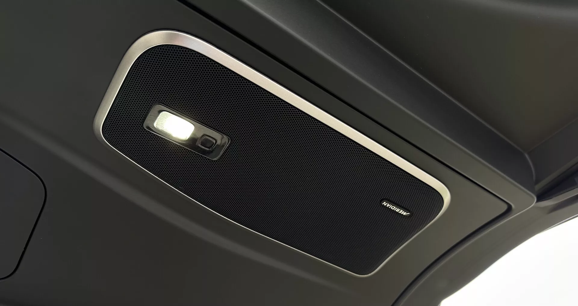 Detailní pohled na horní konzoli interiéru Range Roveru 2021, prezentující vysoce kvalitní mřížku reproduktoru a stropní světlo, zdůrazňující prémiovou akustiku kabiny a pokročilou technologii interiérového osvětlení.