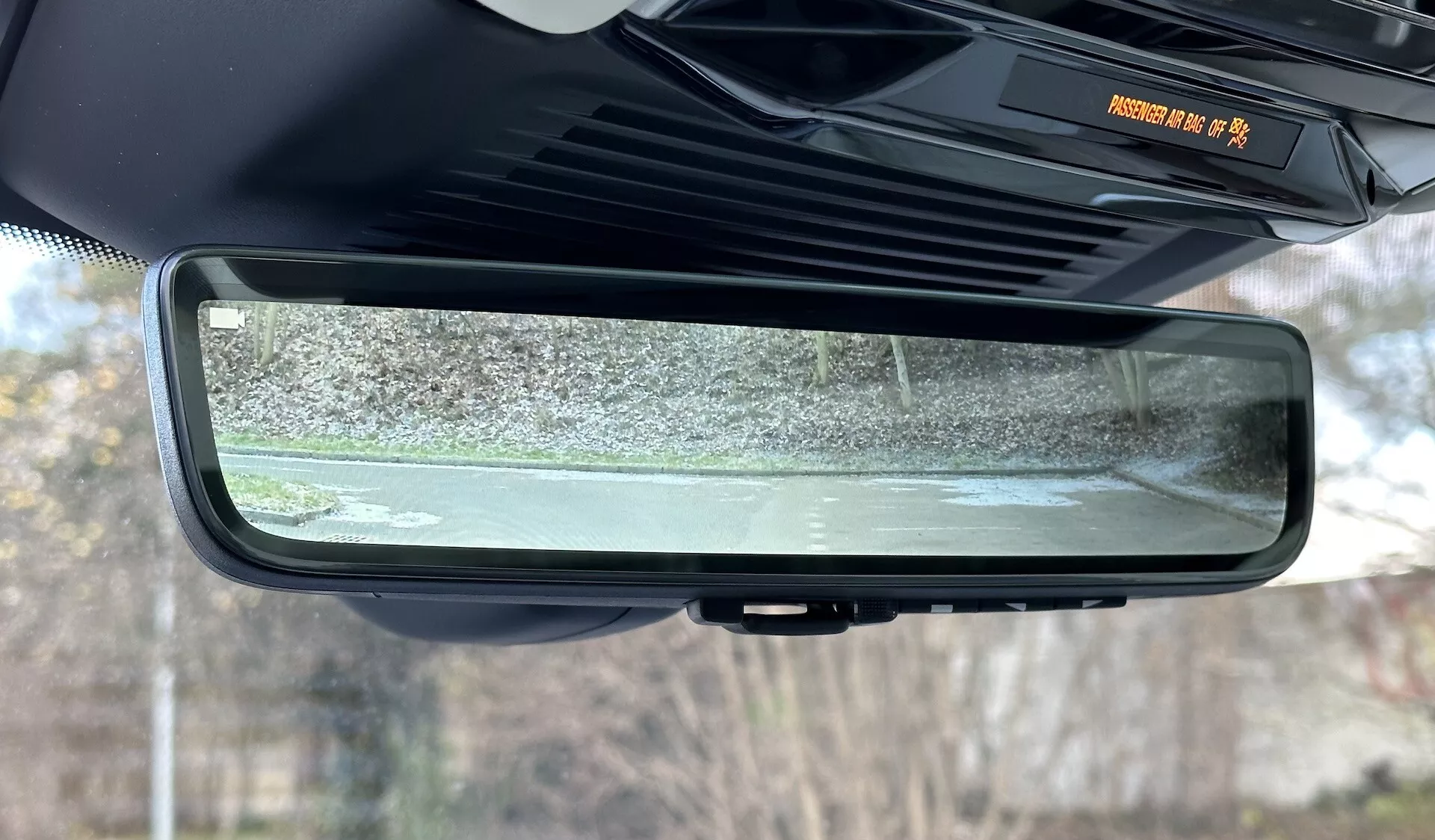 Detailní pohled na elektrochromatické samo-zatmavovací zpětné zrcátko uvnitř Range Roveru 2021, zdůrazňující jeho bezrámový design, prvky interiéru kabiny a odráženou scénu statického venkovního prostředí