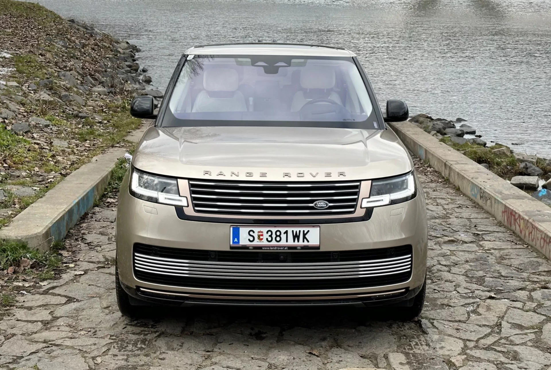 Range Rover 2021 ve světlé metalické barvě, pohled zepředu ukazuje mřížku, LED světlomety, parkovací senzory a kameru směřující dopředu, zaparkovaný na dlažebních kostkách