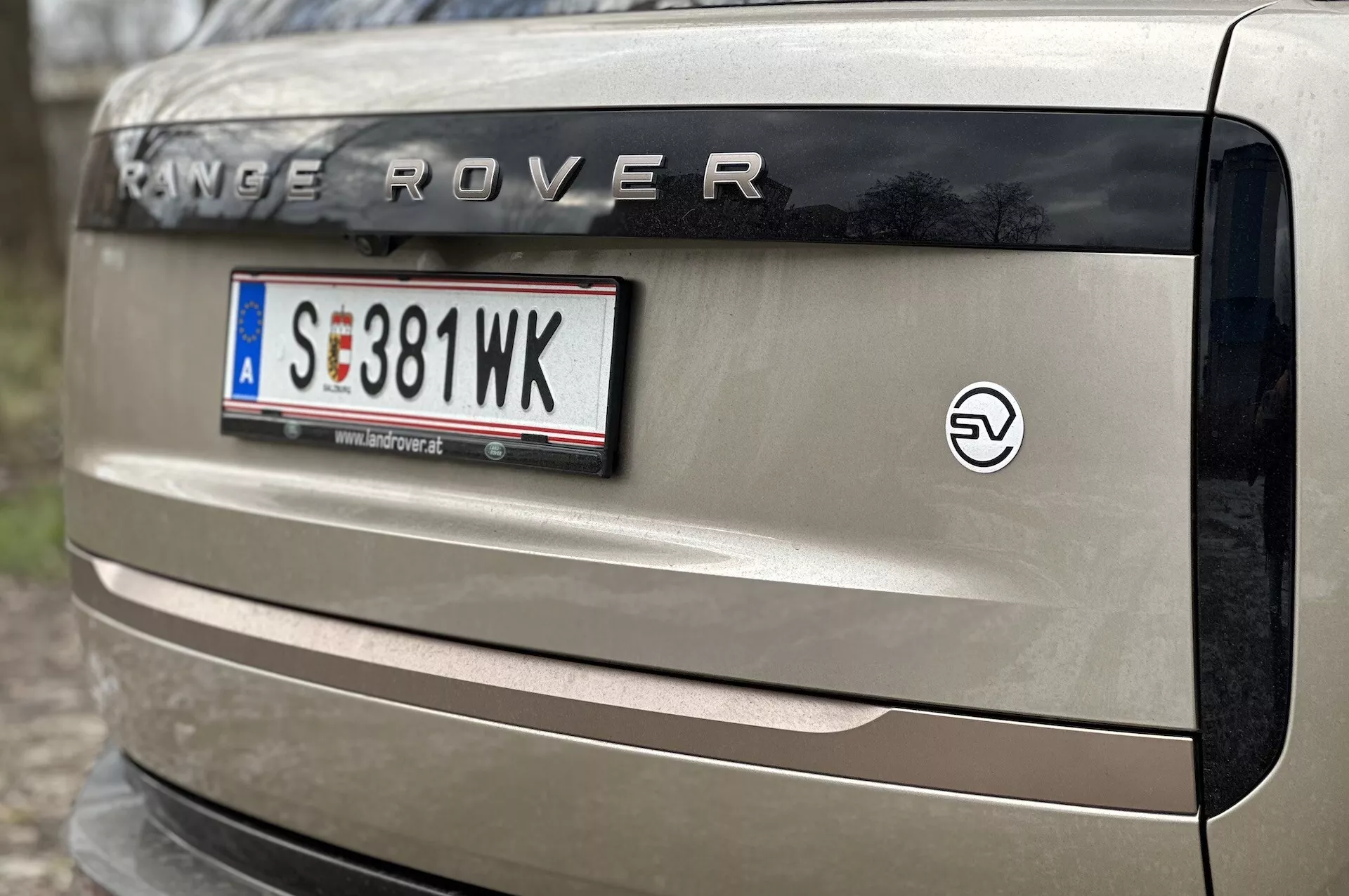 Detailní pohled na zadek vozidla Range Rover 2021 s nápisem 'RANGE ROVER', evropským držákem registrační značky, znakem pro elektrický pohon a částí zadního světla