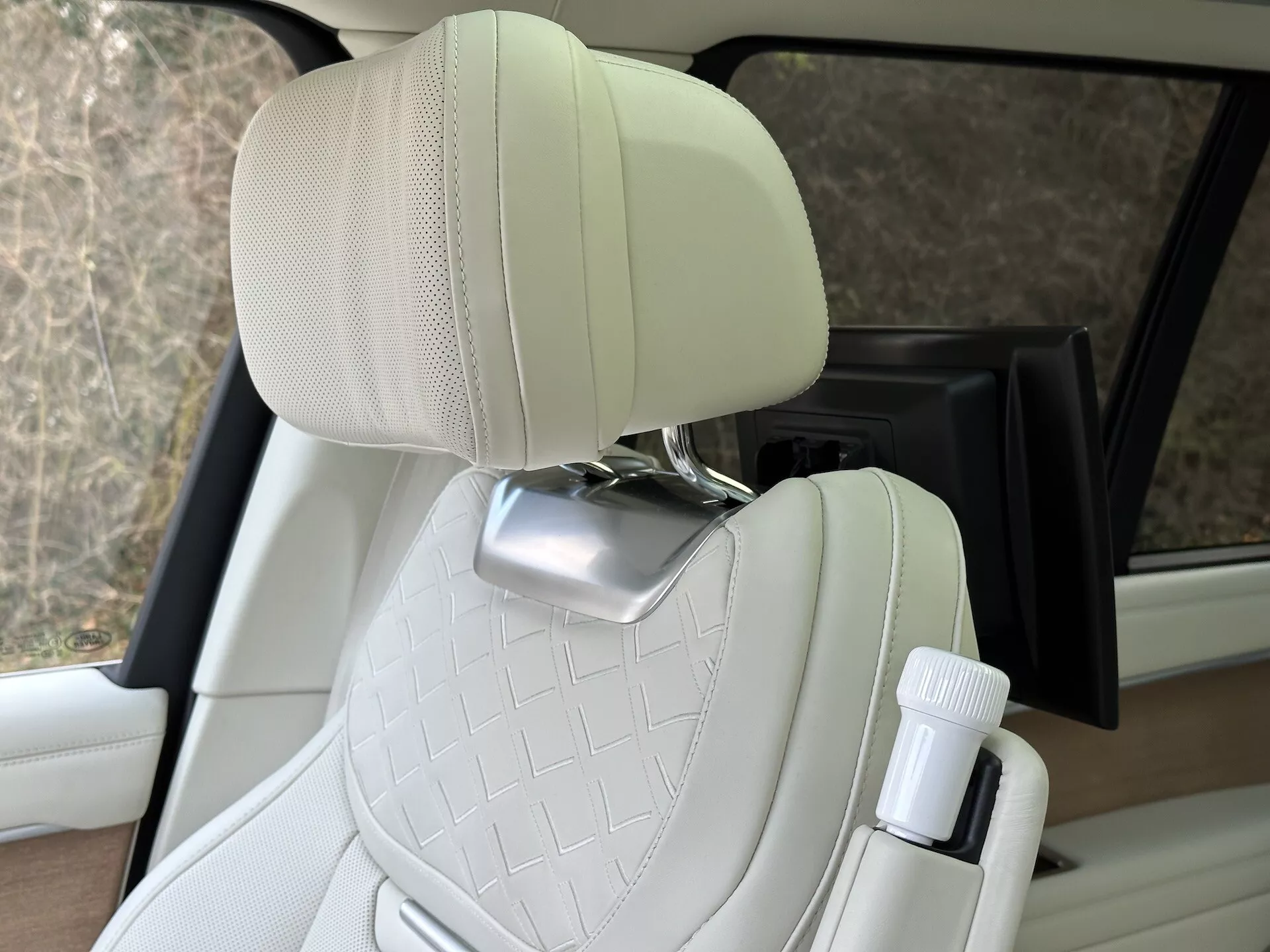 Interiér Land Rover Range Rover 2021 s výrazným prošívaným cestujícím sedadlem z krémové kůže s chromovanou opěrkou hlavy a držákem na láhev u dveří, předvádějící design luxusních vozidel a pohodlné funkce