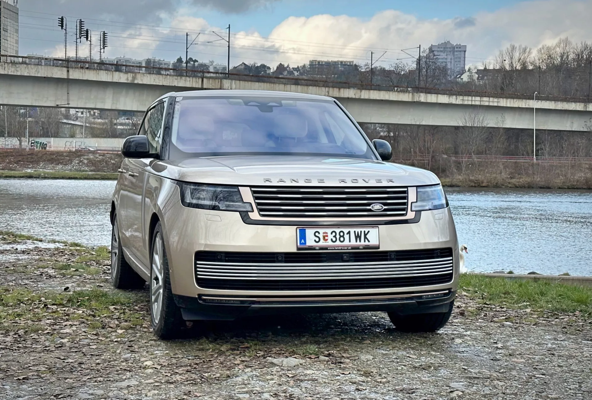 Luxusní SUV Range Rover 2021 zaparkované venku u řeky a mostu v městském prostředí, předvádějící jeho moderní design, přední mřížku a elegantní LED světlomety