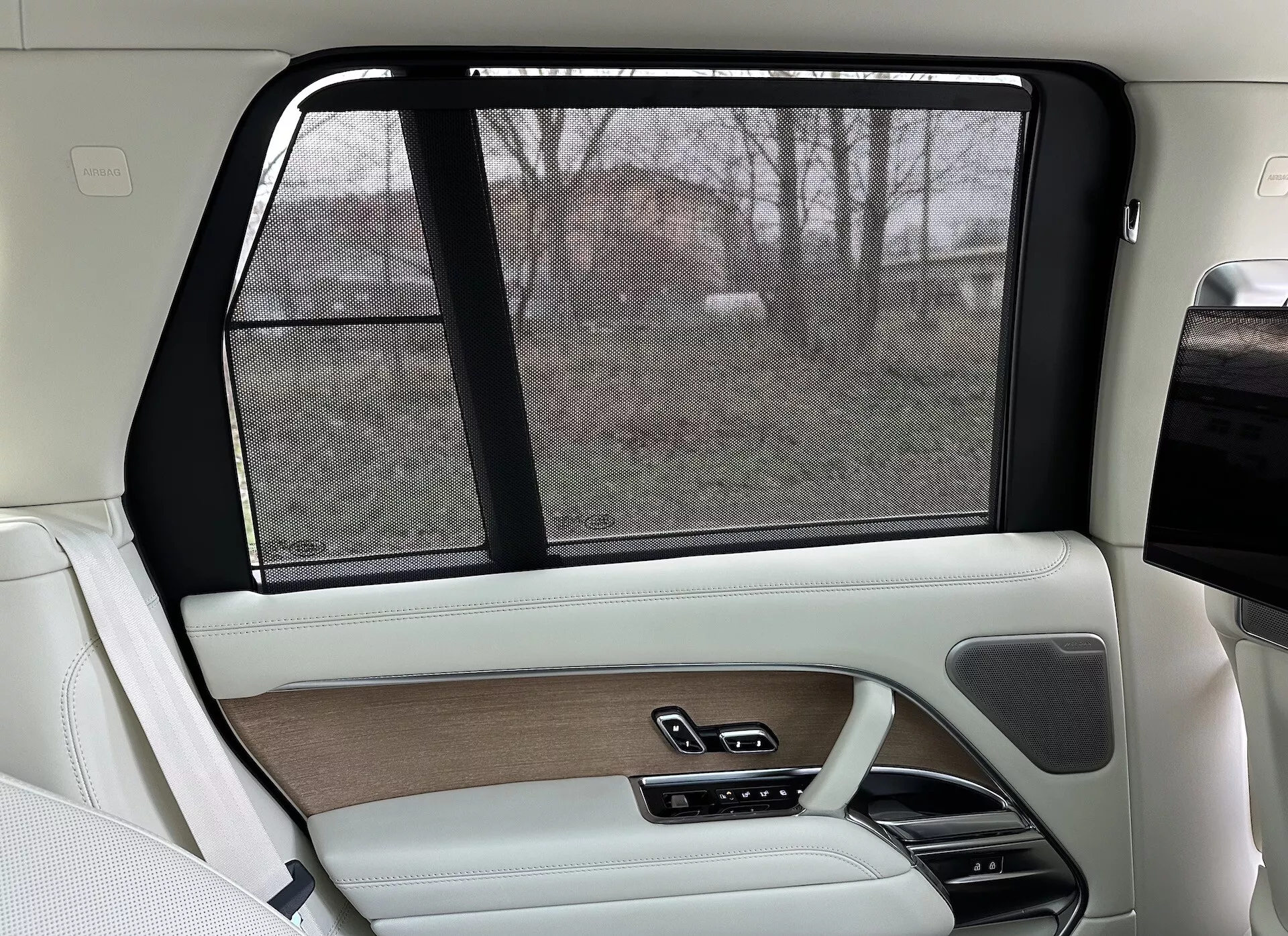 Interiér zadní pravé strany Land Rover Range Rover 2021, s luxusním designem v béžové a černé, dřevěnými obloženími, koženými povrchy, elektronickou sluneční clonou a pokročilými ovládacími systémy