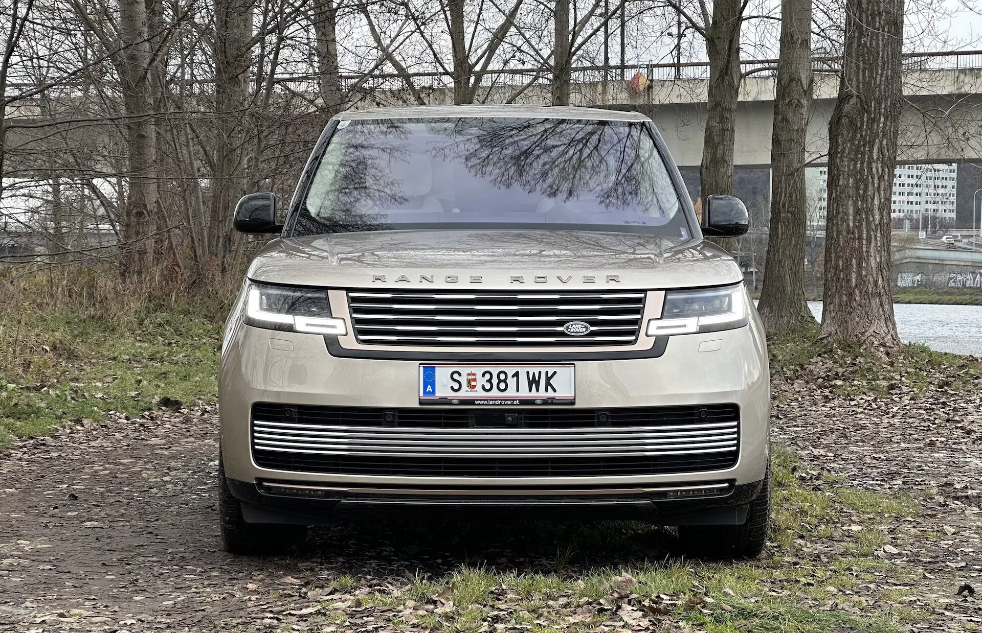 Přední pohled na Range Rover 2021 ukazující mřížku, LED světlomety, nápis 'RANGE ROVER' na kapotě a zaparkovaný na nezpevněném povrchu se semi-venkovským pozadím