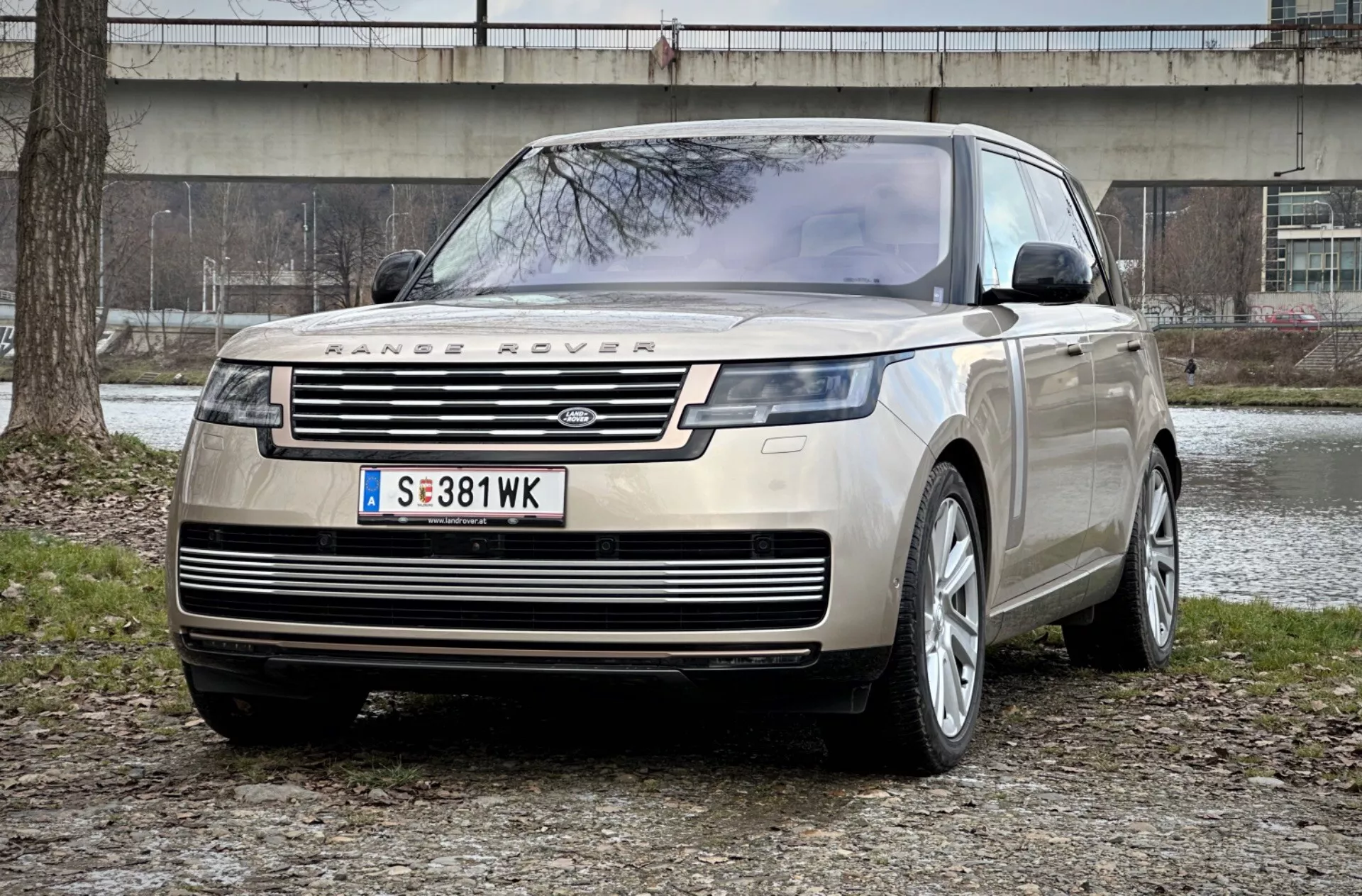 Range Rover 2021 v působivém pohledu z předního tříčtvrtečního úhlu, který zdůrazňuje jeho charakteristickou přední mřížku, elegantní LED světlomety a robustní přední ochranný plech proti pozadí městského parku, což zdůrazňuje luxus a schopnosti v terénu.