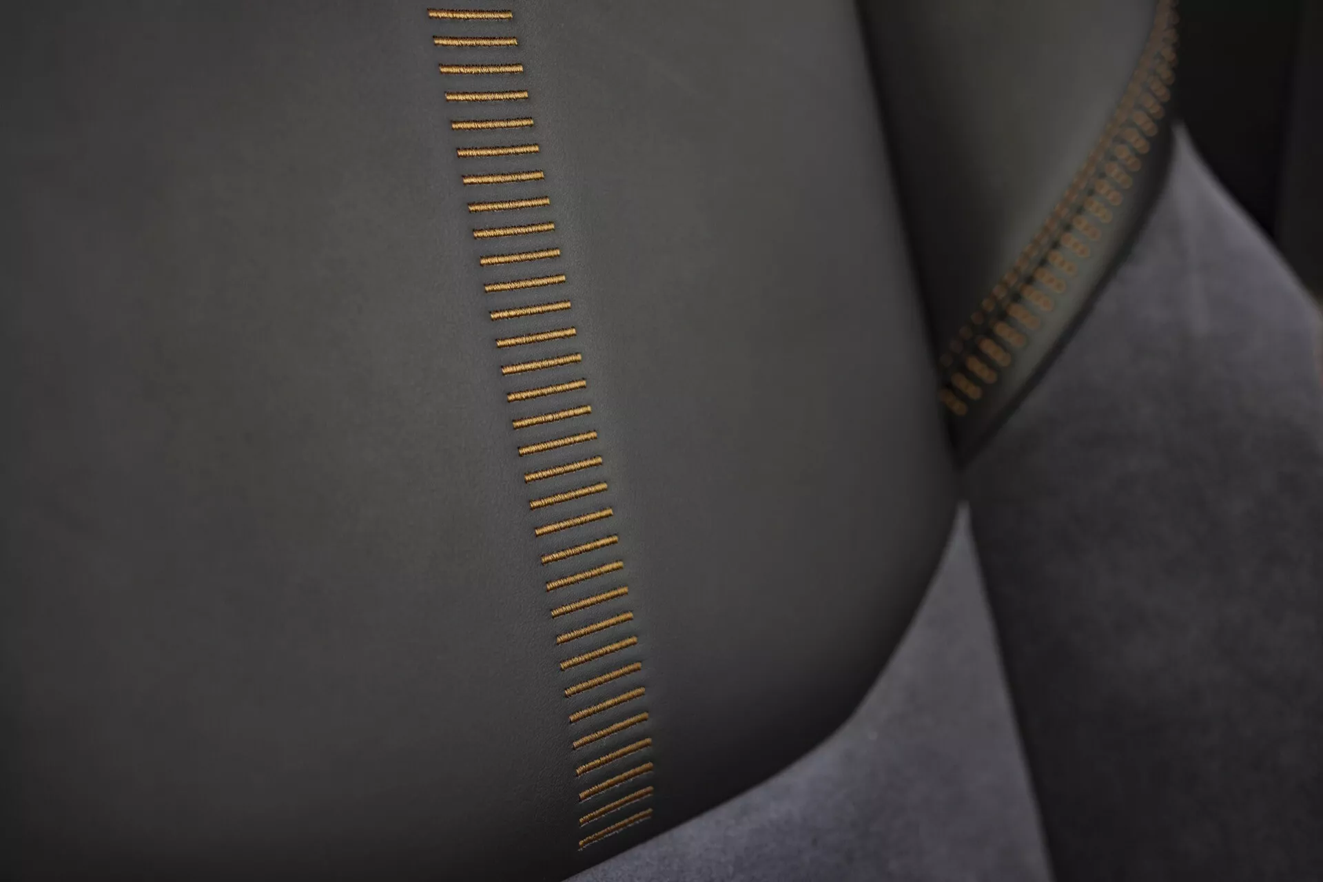Detailní pohled na zuby zipu vysoké kvality s detailním prošíváním na hladké látce podobné semišu a kovové části v zlatém tónu odrážející světlo