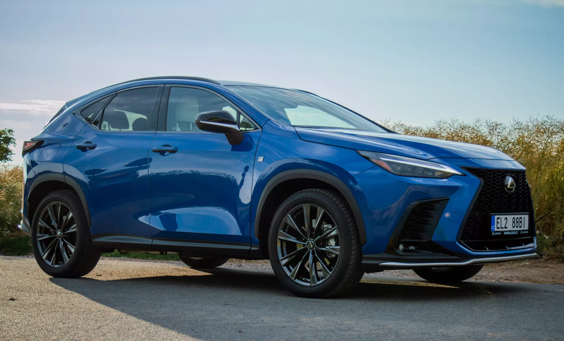 Kompaktní SUV Lexus NX 2021 ve výrazné modré barvě, předvádějící přední nárazník, mřížku, LED světlomety, kapotu, kola a linie bočních kontur z pohledu ze tří čtvrtin zepředu venku ve dne