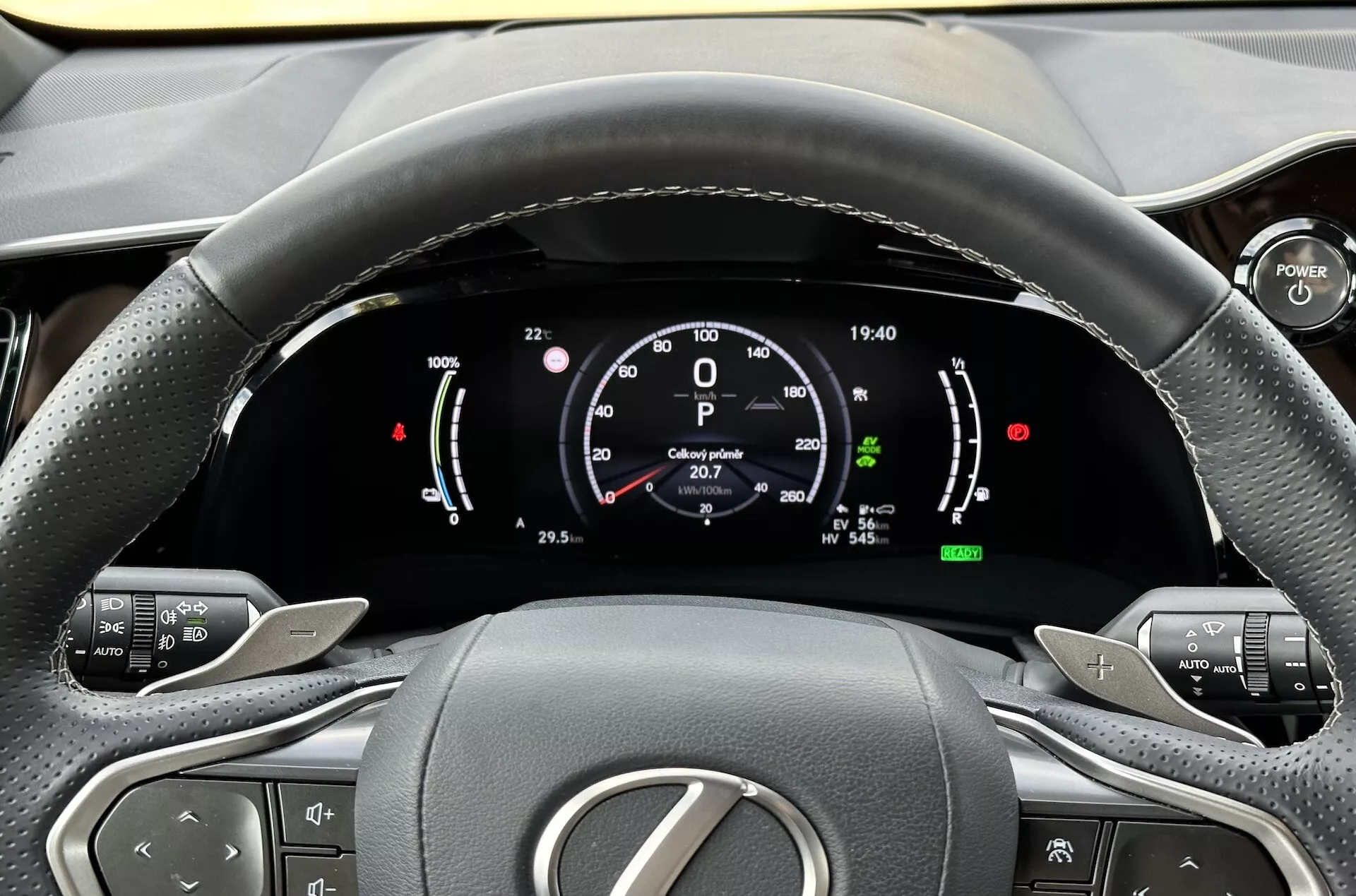 Pohled z místa řidiče na volant a digitální přístrojový panel Lexus NX 2021, zdůraznění ukazatelů hybridní technologie, tlačítek pro ovládání komfortu a ergonomického designu interiéru