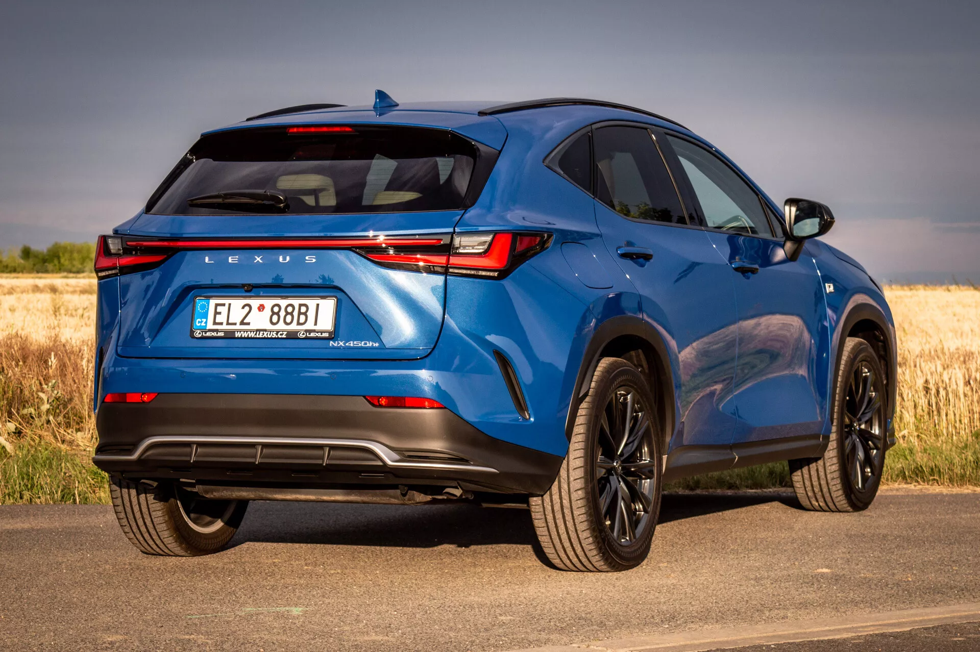 Modrý SUV Lexus NX 2021 v záběru ze zadního tříčtvrtečního úhlu představující designové prvky a technologické funkce na slunný den s přírodním pozadím
