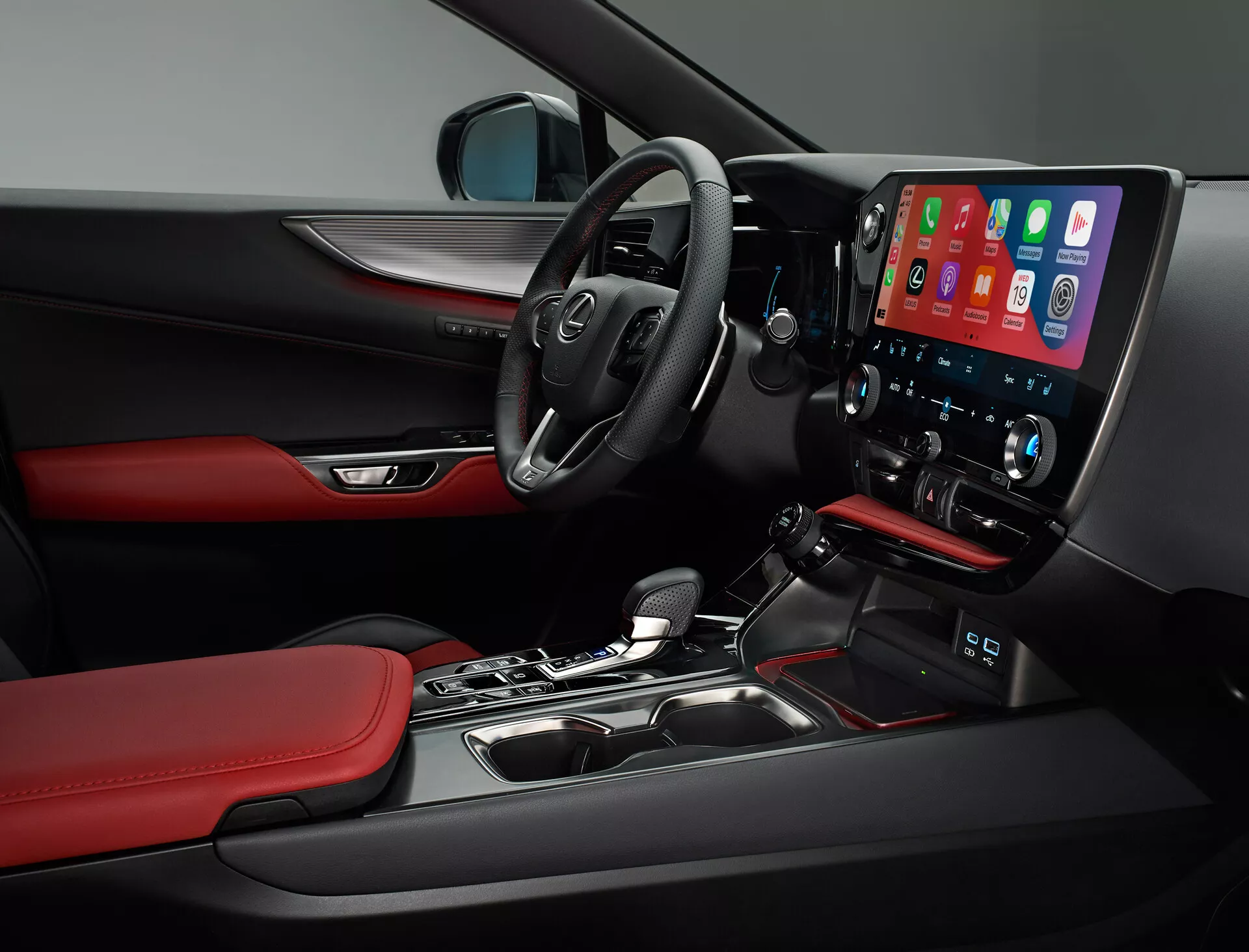 Pohled do interiéru Lexus NX 2021 ukazuje stranu řidiče. Obrázek zachycuje multifunkční volant s ovládacími prvky, částečně viditelnou palubní desku a výraznou centrální konzoli s velkou vertikální dotykovou obrazovkou infotainmentu, pravděpodobně zobrazující Apple CarPlay. Pod obrazovkou jsou ovladače klimatizace pro dvě zóny. Automatická řadicí páka, materiály a designové detaily jako černé povrchy s červenými akcenty na sedadlech a výplních dveří, a částečný pohled na ovládací prvky na dveřích řidiče odrážejí sportovní a prémiový charakter vozidla.