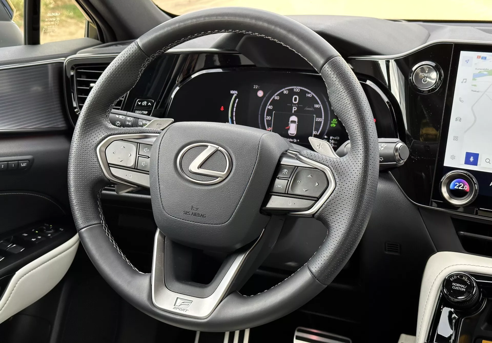 Interiérový pohled na Lexus NX 2021 se zaměřením na volant a palubní desku, prezentující multifunkční tlačítka, digitální přístrojový panel, dotykovou obrazovku infotainmentu, kožené akcenty, volič režimu jízdy, vzduchové mřížky a detailní prošívání.