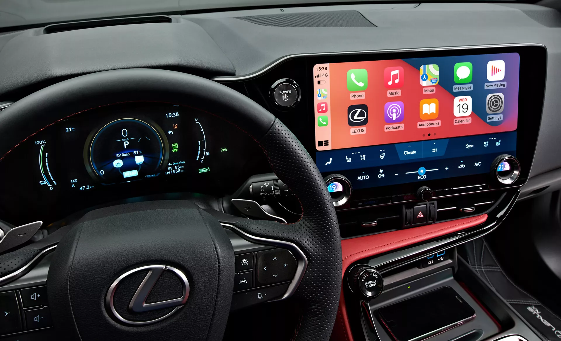 Interiér vozu Lexus NX 2021 ukazující moderní, vysoce technologický přístrojový panel z pohledu řidiče. Vlevo je částečně viditelné volant s logem Lexus a multifunkčními tlačítky. Digitální přístrojová deska zobrazuje rychlost, otáčky a další metriky v modré a bílé barvě. Uprostřed vertikálně umístěný široký dotykový infotainment systém, který integruje funkčnosti chytrých telefonů. Pod ním jsou tlačítka a číselníky klimatizace s digitálními displeji teploty. Dolní část obsahuje koženě šitý středový panel s řadicí pákou a konektory, které odrážejí luxusní provedení vozu.