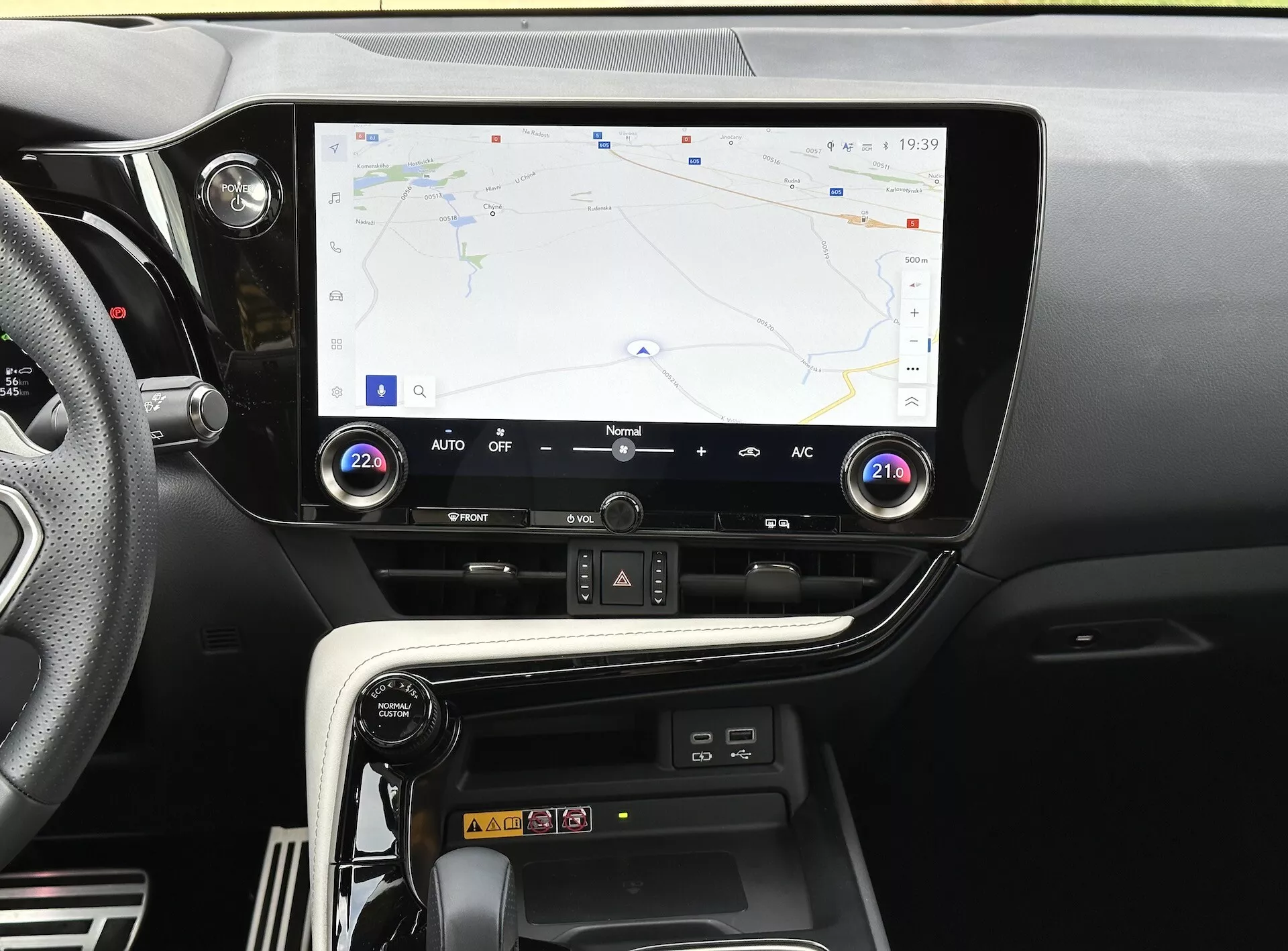 Středová konzole Lexus NX 2021 s dotykovým displejem zobrazujícím GPS navigaci, tlačítka a ovladače klimatizace a oddíl pro bezdrátové nabíjení smartphonu