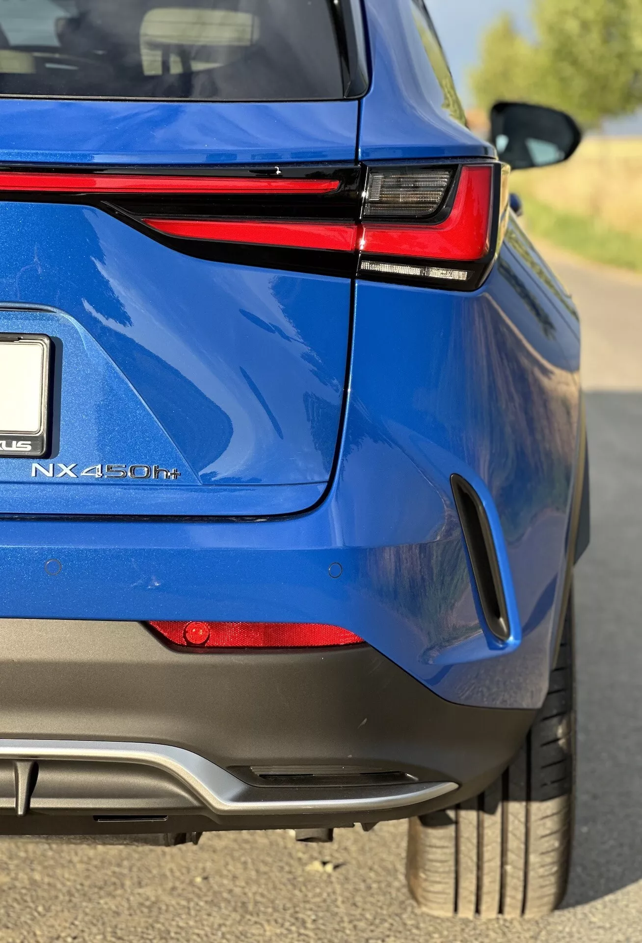 Detailní úhlový pohled na zadní část modrého hybridního SUV Lexus NX 450h+, zdůrazňující jeho lesklý povrch, LED zadní světla, hybridní označení a sportovně laděné designové prvky