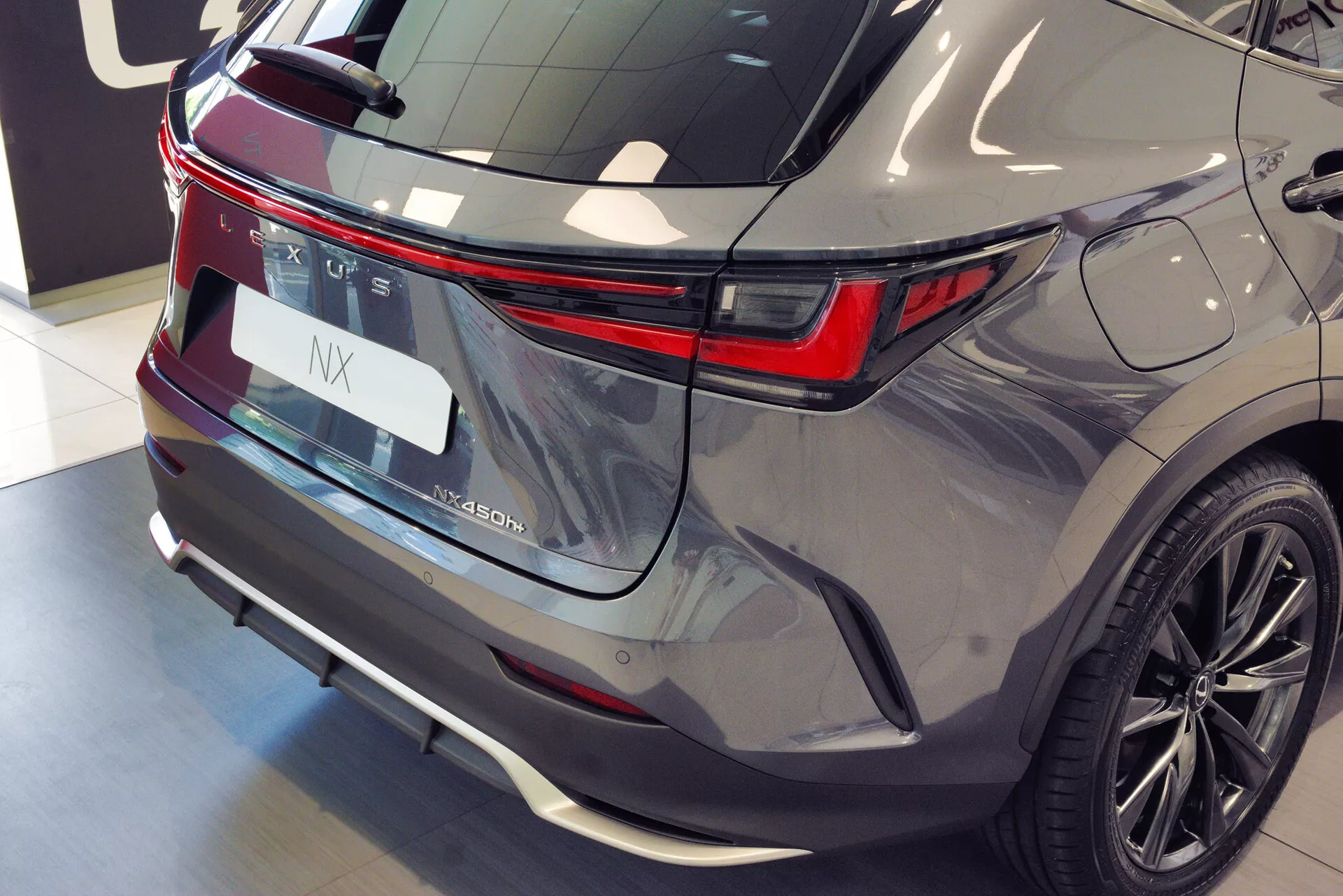 Tento obrázek ukazuje moderní SUV z pohledu tříčtvrtinového zadního pohledu, zdůrazňujícího konec vozidla. Auto stojí s pravou zadní stranou blíže k fotoaparátu, což poskytuje jasný pohled na prvky jako střešní spoiler, zadní okno se stěračem a výraznou horizontální LED světelnou lištu táhnoucí se přes šířku vozidla. Emblém výrobce a označení modelu jsou jasně zobrazeny na spodní části víka kufru a vyhrazené místo pro registrační značku je lemováno chromovým proužkem. Zadní nárazník vyčnívá směrem ven a možná ukrývá parkovací senzory a kameru. Kovový lak se září pod osvětlením showroomu a viditelný je víceřádkový design slitinového kola zadního kola. Vozidlo je pravděpodobně prezentováno v showroomu, zdůrazňující jeho design luxusního SUV.