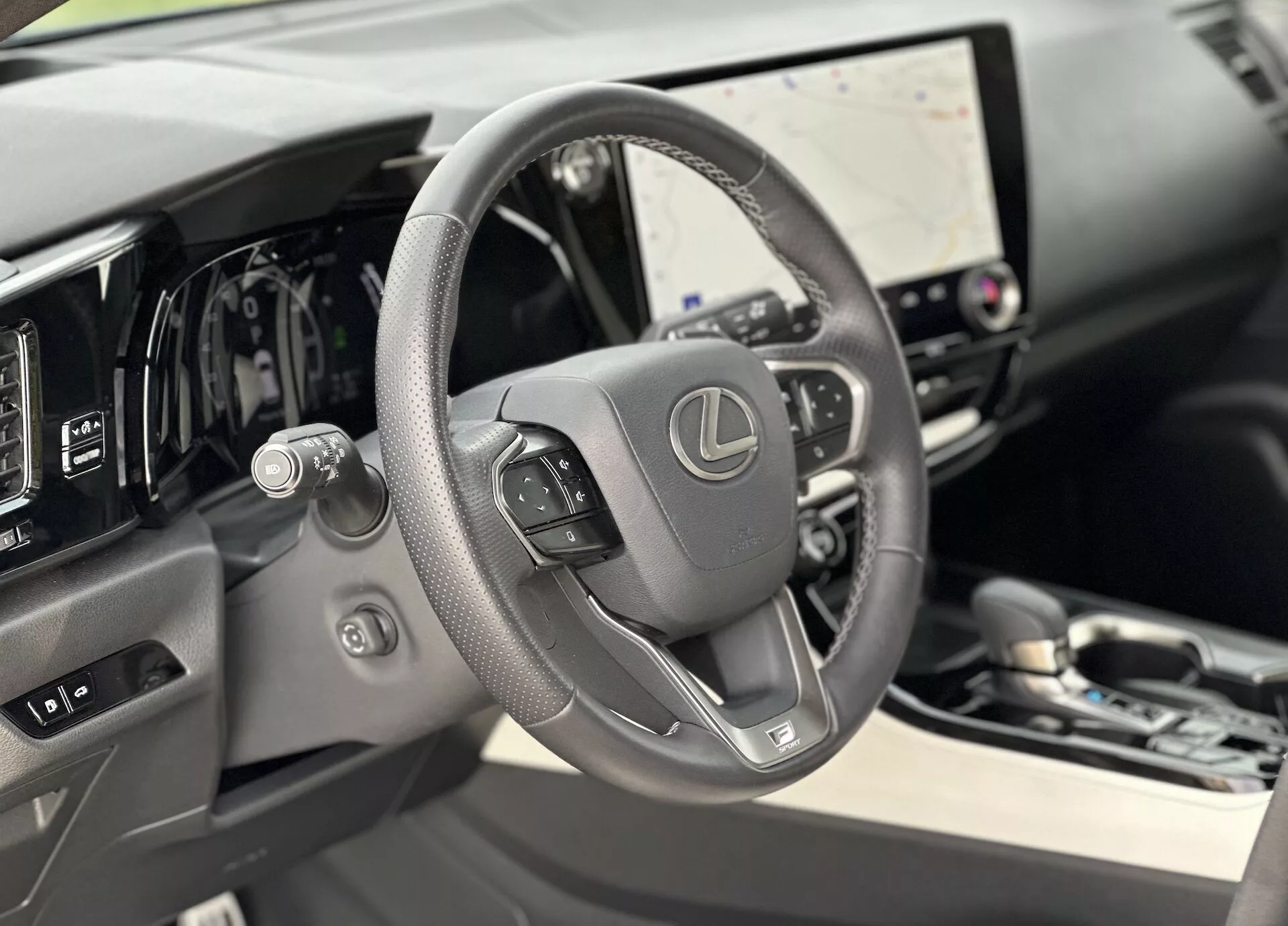 Pohled do interiéru Lexusu NX 2021 se zaměřením na kožený volant s ovládáním a digitální palubní desku za ním, s velkou dotykovou obrazovkou infotainmentu a nenápadnými náznaky luxusu ve vysoce kvalitních materiálech